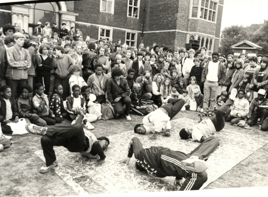 Break dancers, Charlton House, 1983: Break dancers perform on a mat in the grounds of Charlton House while a large crowd of adults and children watches from around the lawn.