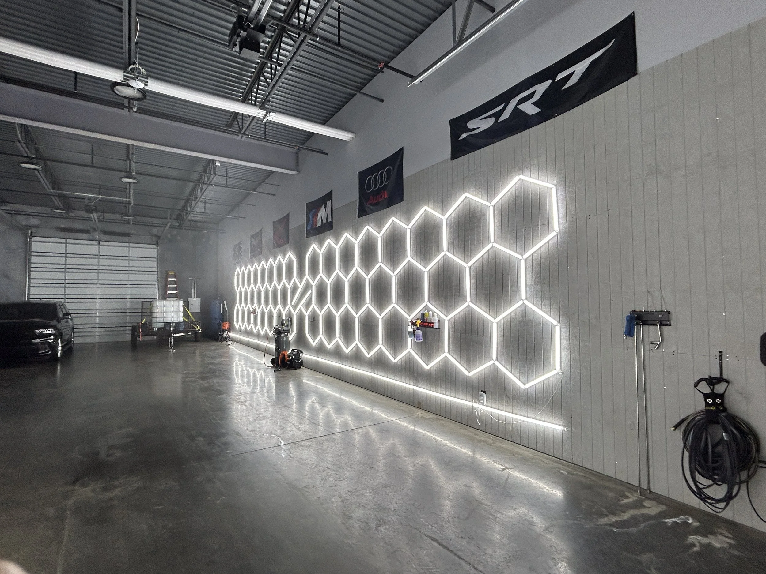 Photo of an indoor garage with a wall decorated with a glowing hexagonal pattern, flags hanging from the ceiling, and various garage equipment and vehicles present.