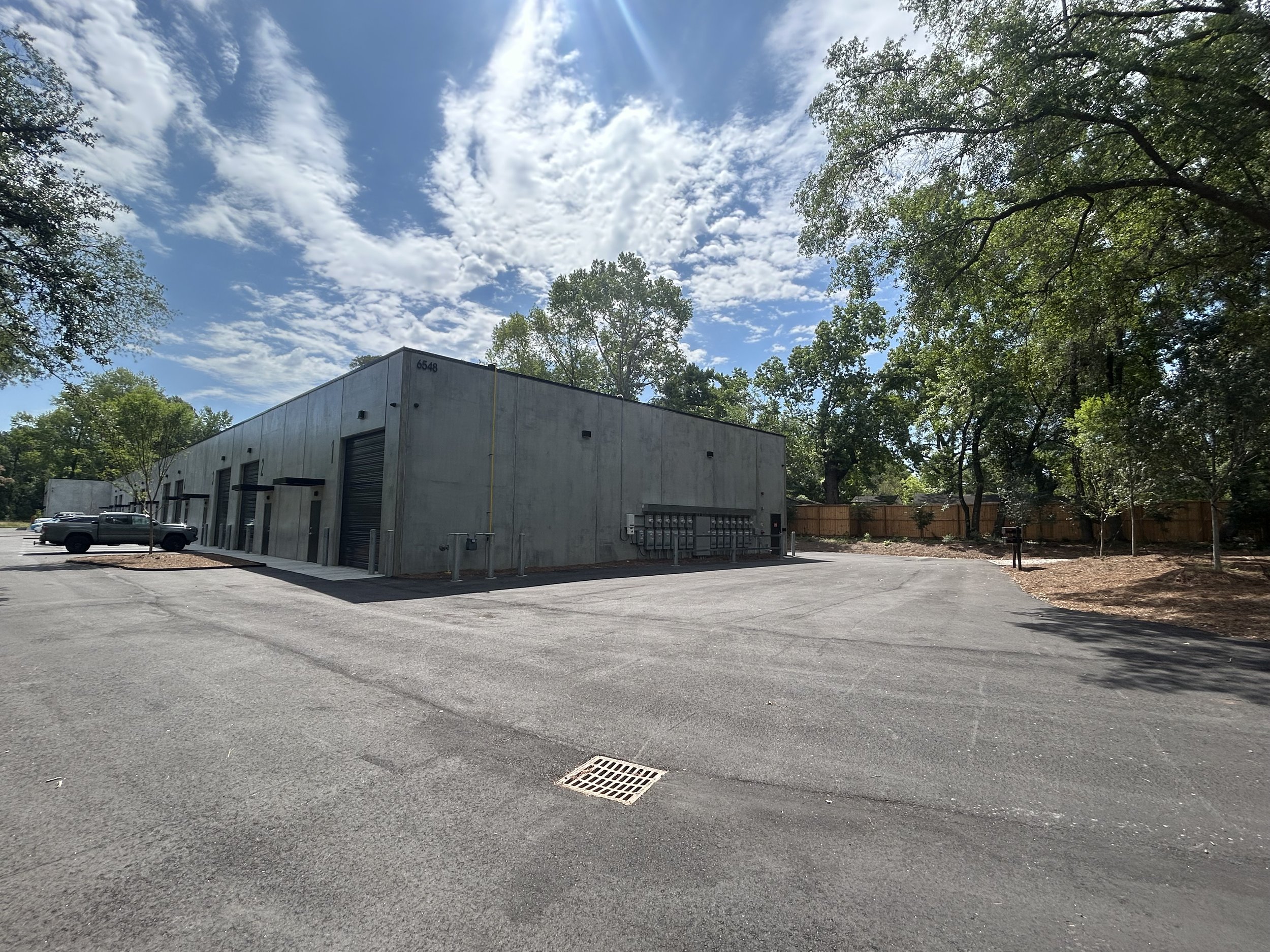 Parking lot with a building on the left, trees and a sky with scattered clouds above.