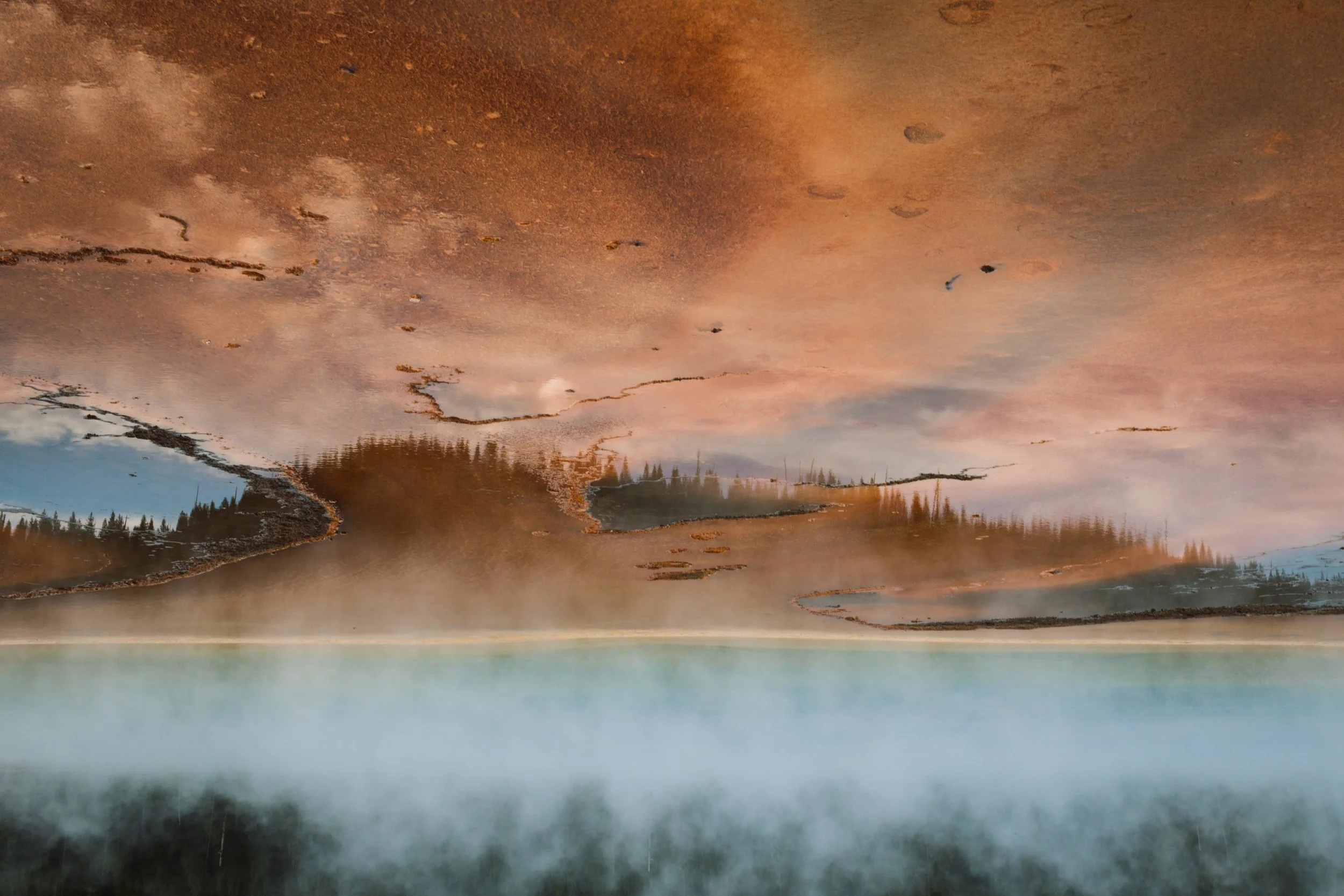 Reflection of a cloudy sky and tall trees in a still lake, with a foggy surface and a misty atmosphere.