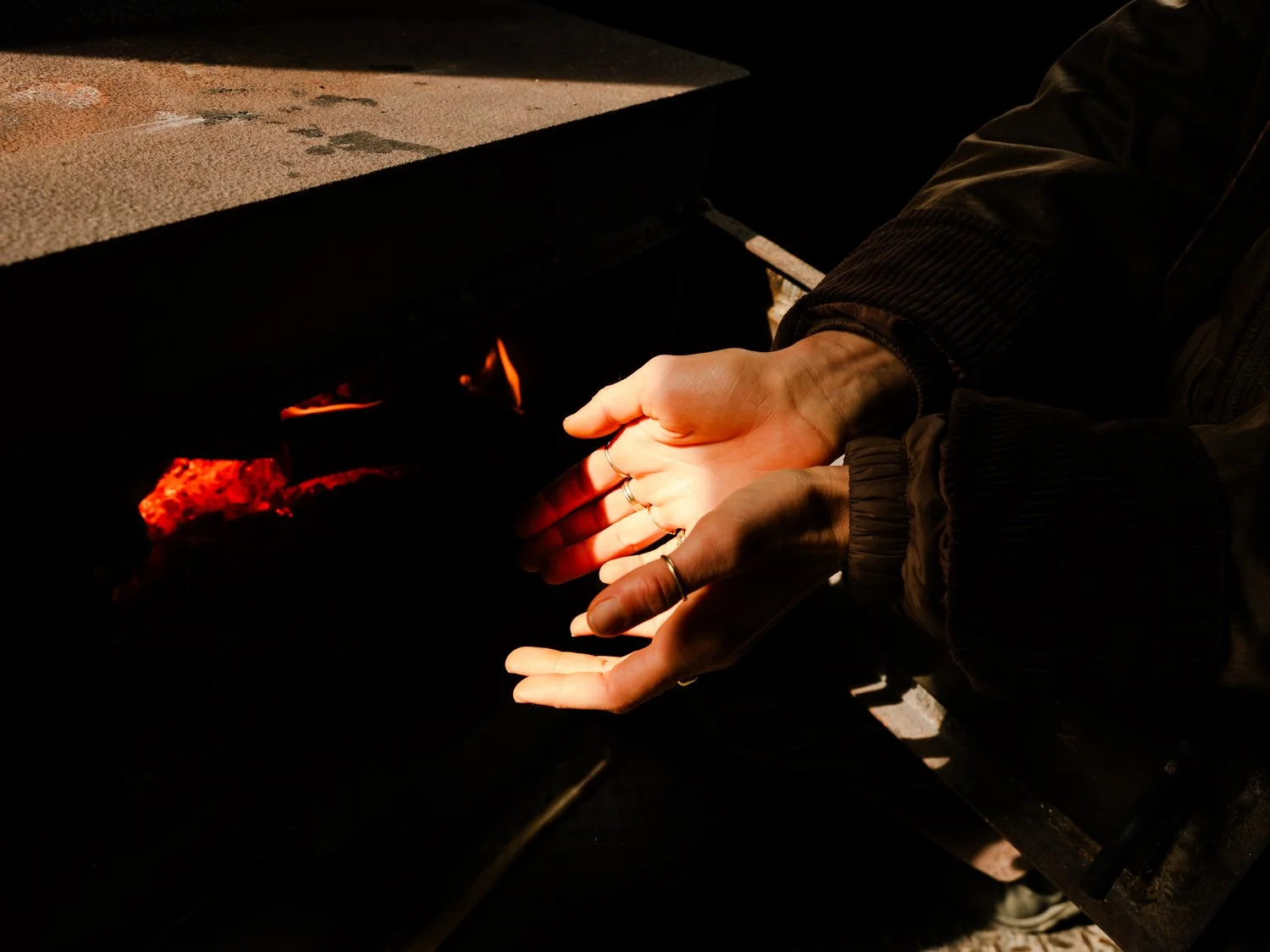 Person with hands covered in rings warming their hands near a fire in a dark setting