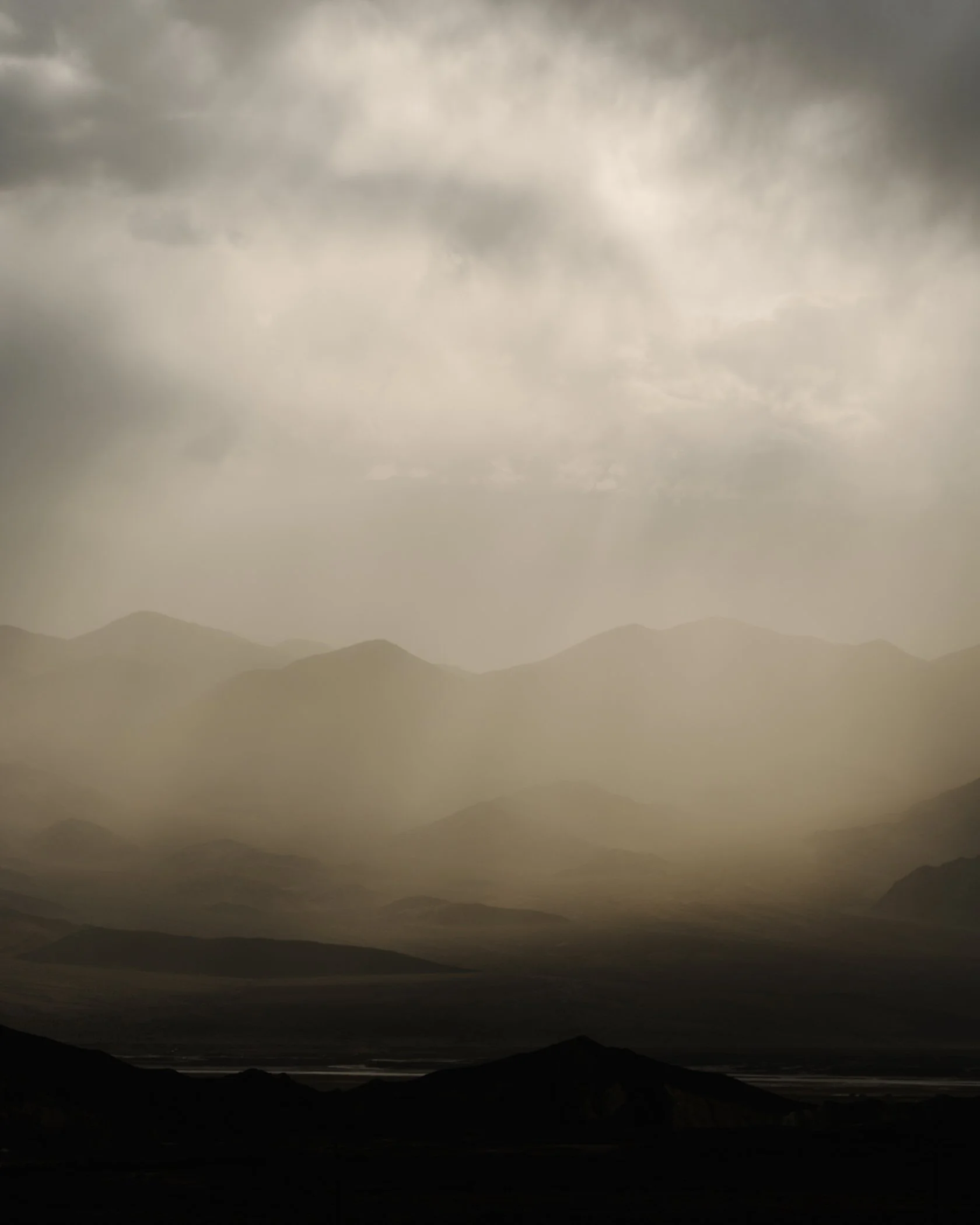 A landscape with mountains and a cloudy sky, with a dark foreground.