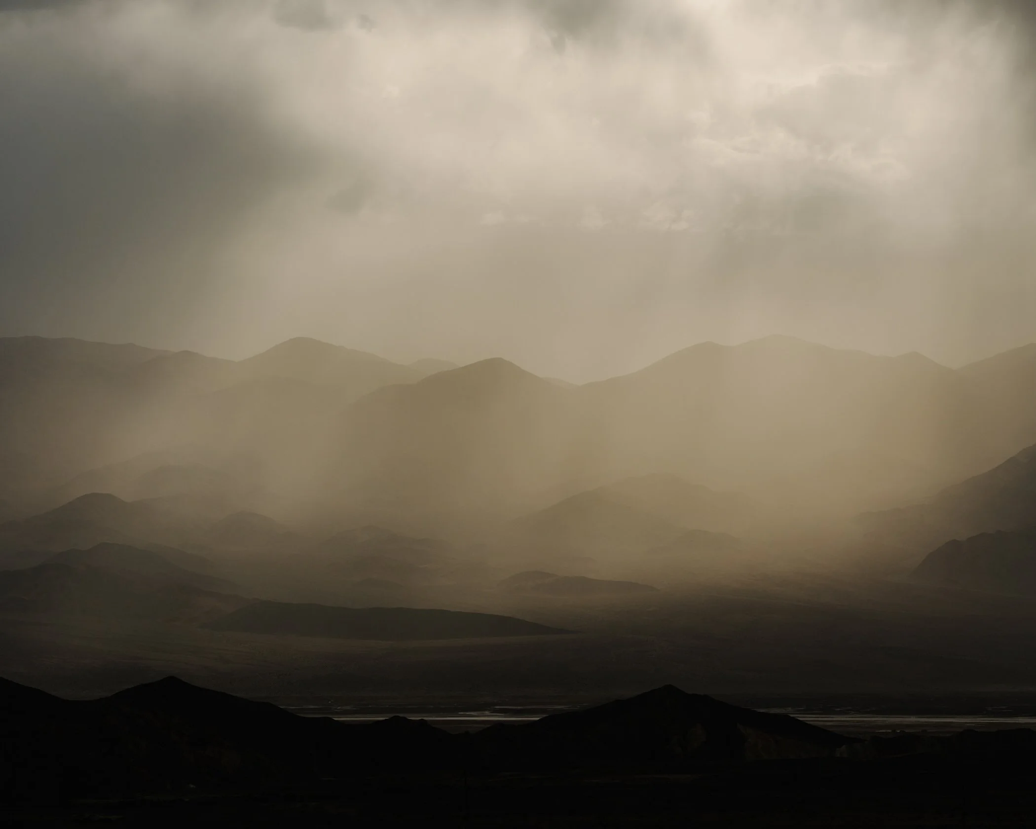 Mountains with hazy sky and clouds, in grayscale or sepia tone.