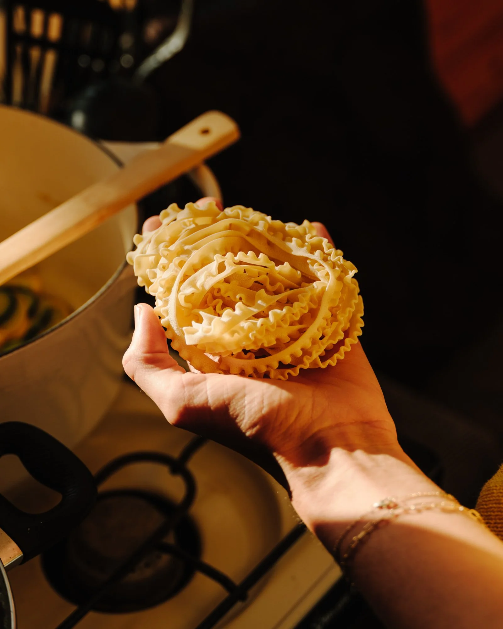 A hand holding a nest of uncooked, ruffled egg noodles over a stove with black burners.