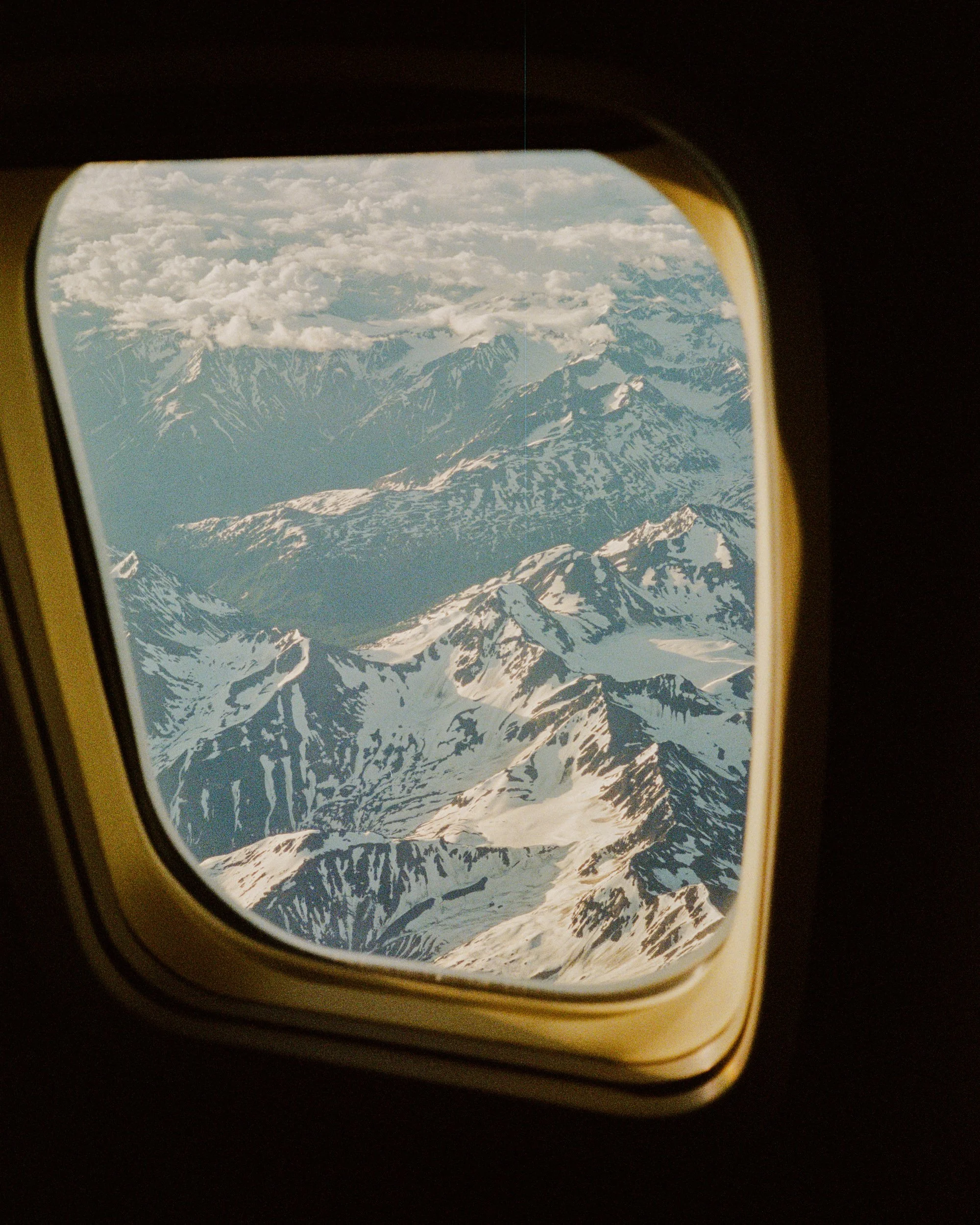 View of snow-capped mountains and clouds through an airplane window.