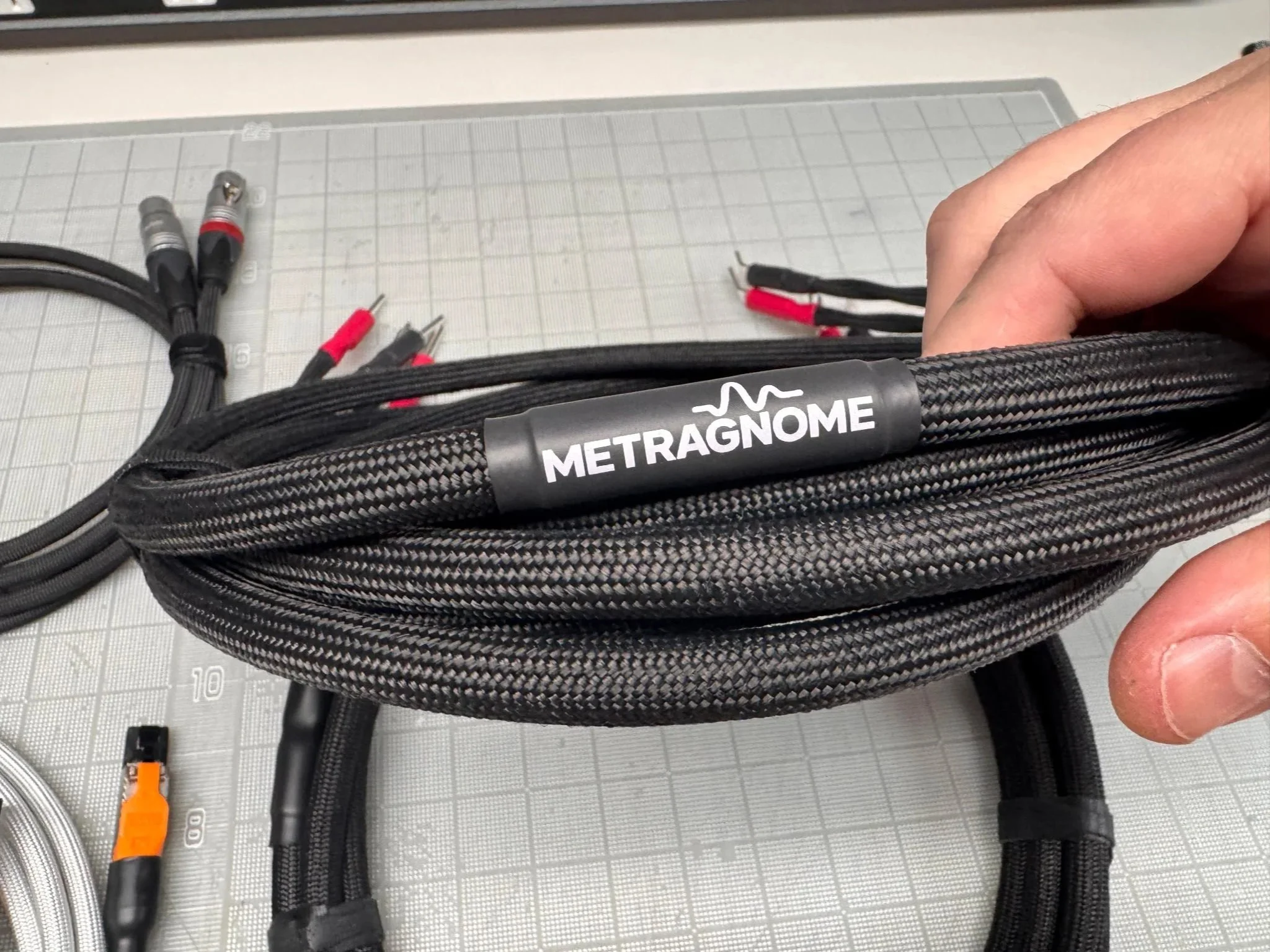 Close-up of a black braided cable with a label 'METRAGOME' and scattered audio or video cables on a gray cutting mat.