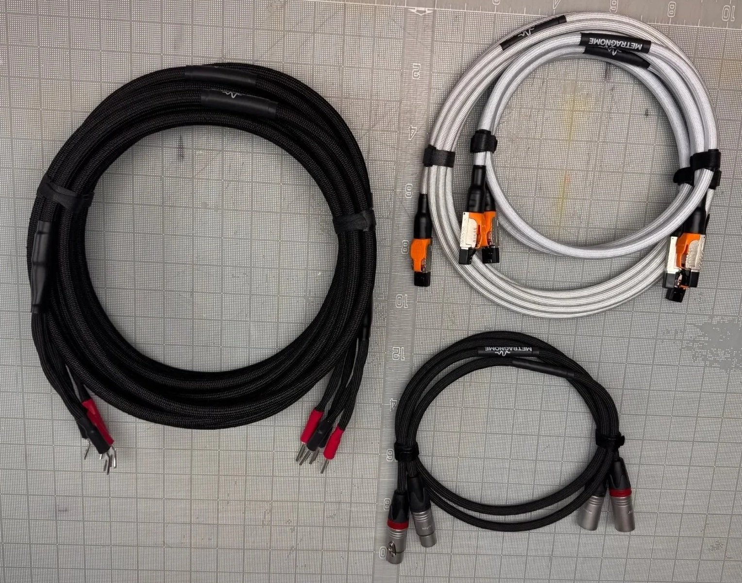Three sets of audio or speaker cables with connectors, two with black cables and one with white cables, laid out on a gray grid cutting mat.