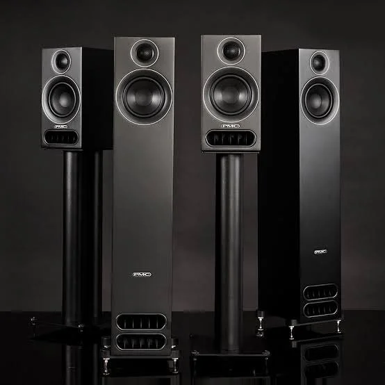 Four floor-standing black and gray stereo speakers arranged in a row on a black background.
