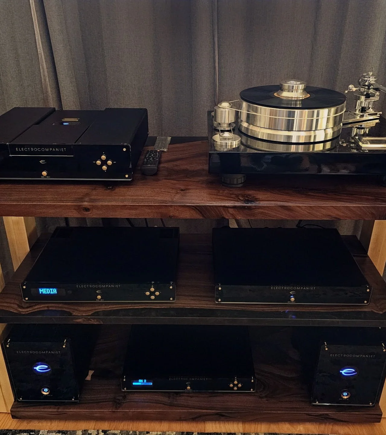 Audio equipment including a turntable, a media player, a preamp, and powered speakers on a wooden shelf.