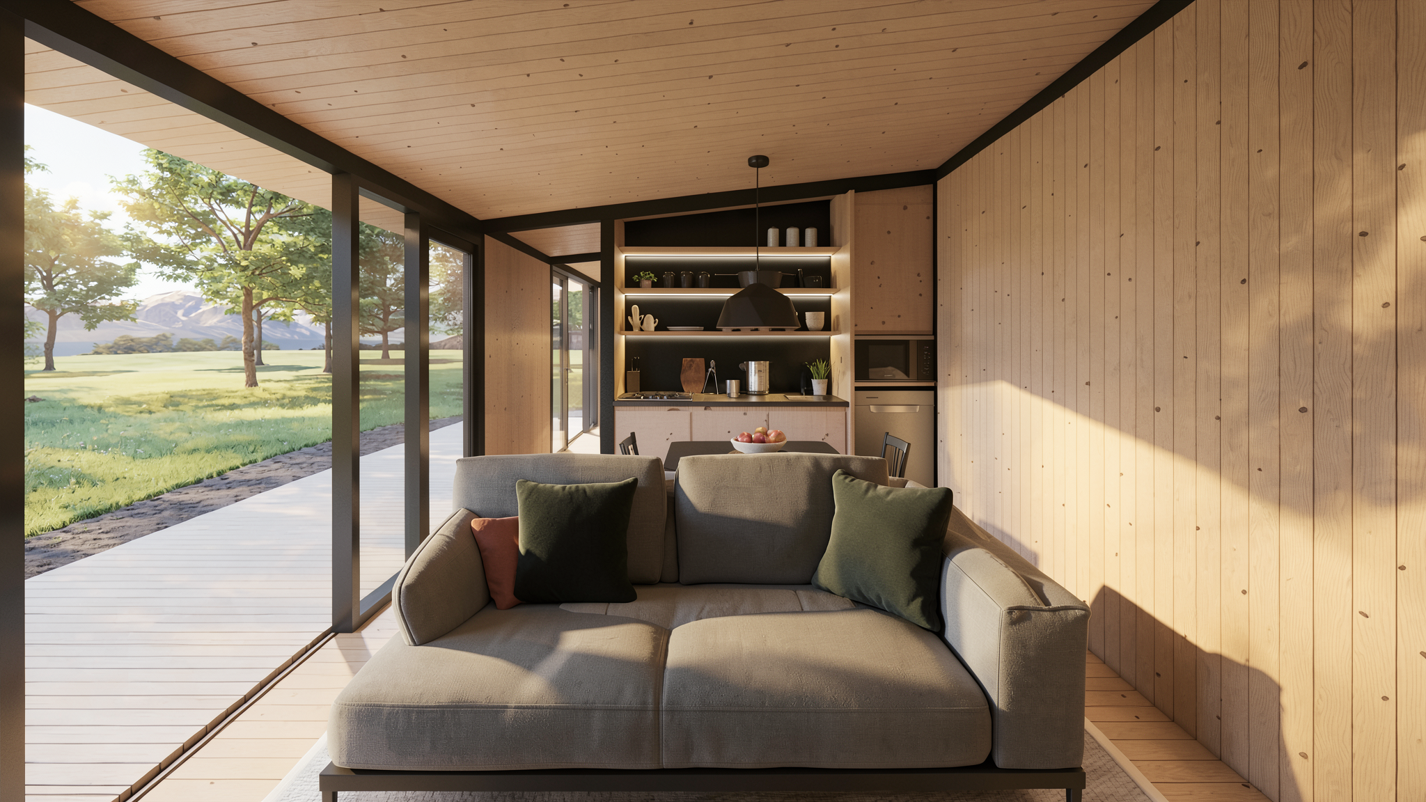 Interior de una sala de estar moderna con paredes y techo de madera, sillón gris con cojines y una vista al exterior de árboles y montañas por grandes ventanas. Cocina en el fondo.