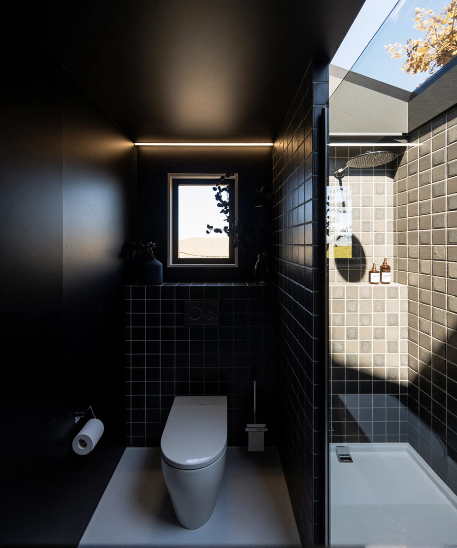 Baño moderno con paredes negras y azulejos oscuros, con un lucernario en el techo, cabaña en el bosque ubicada en España