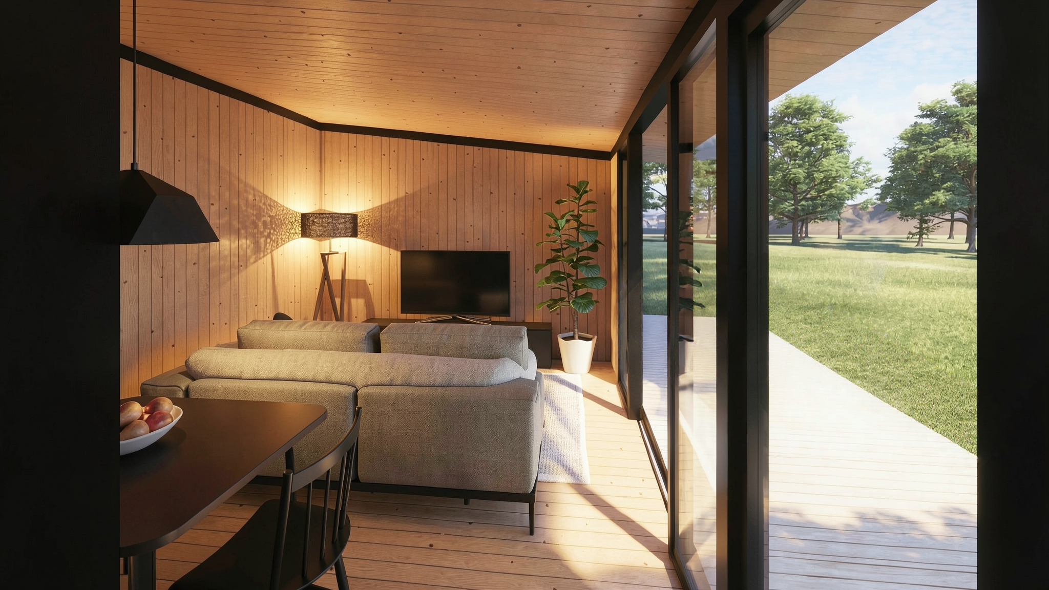 Interior de una sala con paredes y techo de madera, sillón gris, lámpara de pie, TV en una mesa, planta en una maceta blanca y puertas de cristal que muestran un jardín con árboles verdes y césped