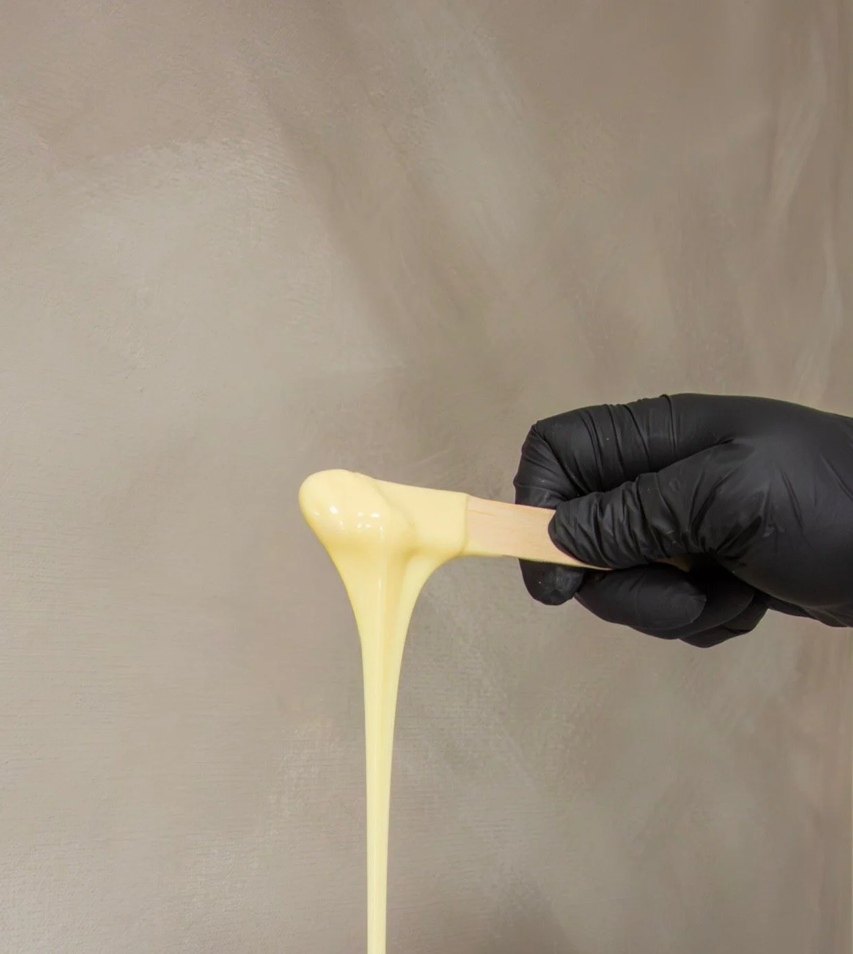 Close-up of hard wax melting from a wooden applicator stick before a waxing treatment