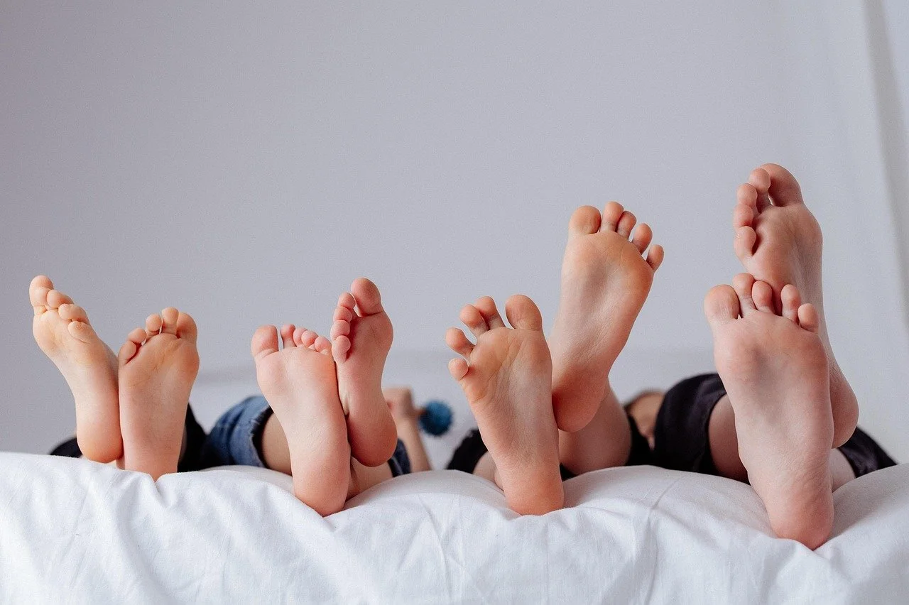 Groupe de plusieurs enfants allongés sur un lit, levant leurs pieds vers la caméra.