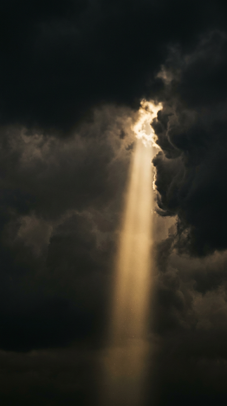 A beam of sunlight breaking through dark, heavy clouds in the sky.