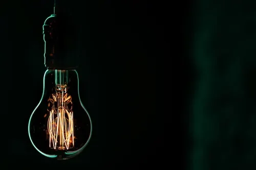 A vintage-style incandescent light bulb hanging in a dark space, lit and glowing with visible filament.