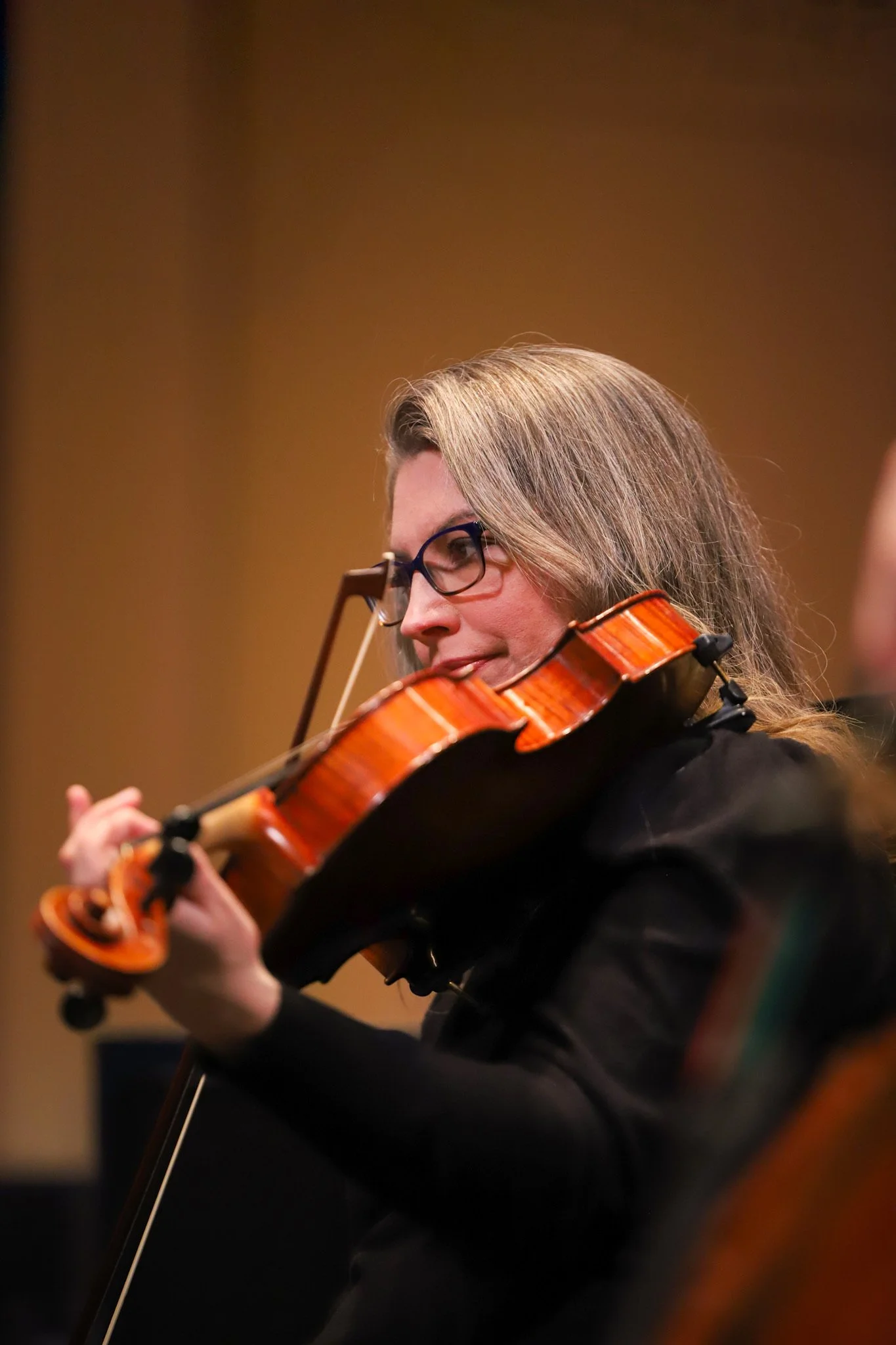 A woman with long blonde hair and glasses playing a violin.