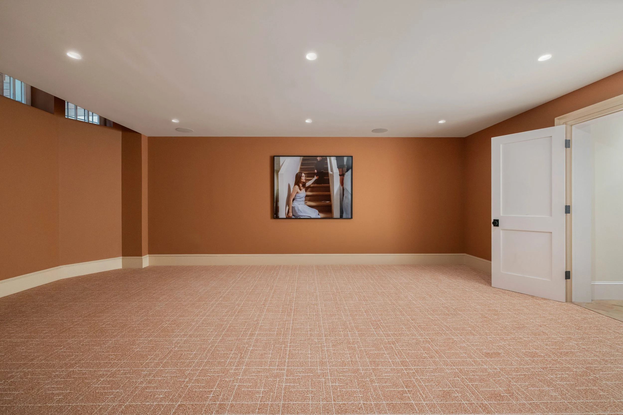 Empty room with beige walls, a framed photo on the wall, brown carpeting, and a partially open white door.