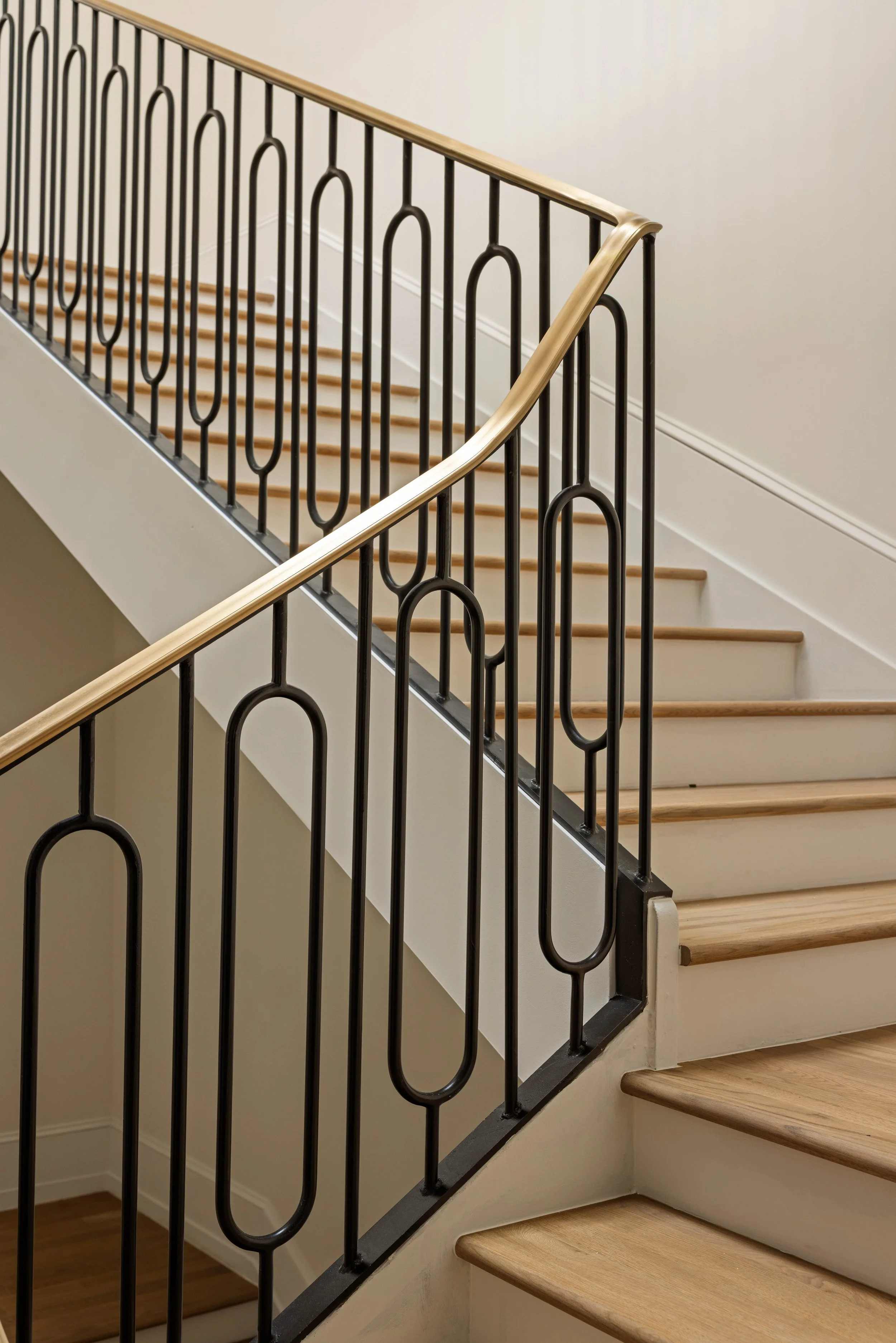 Interior view of a staircase with beige wooden steps and black metal railing with oval and loop designs.