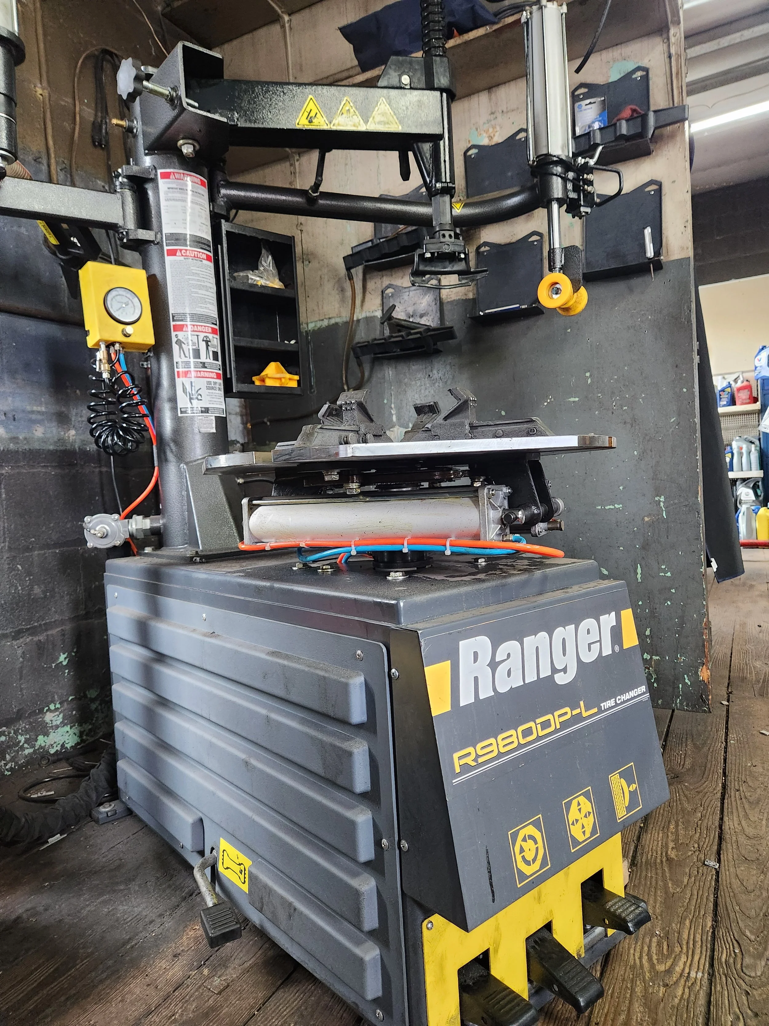 A tire changing machine labeled 'Ranger' situated on a wooden floor in a workshop. It features a control panel, a wheel mounting fixture, and various safety and operational labels.