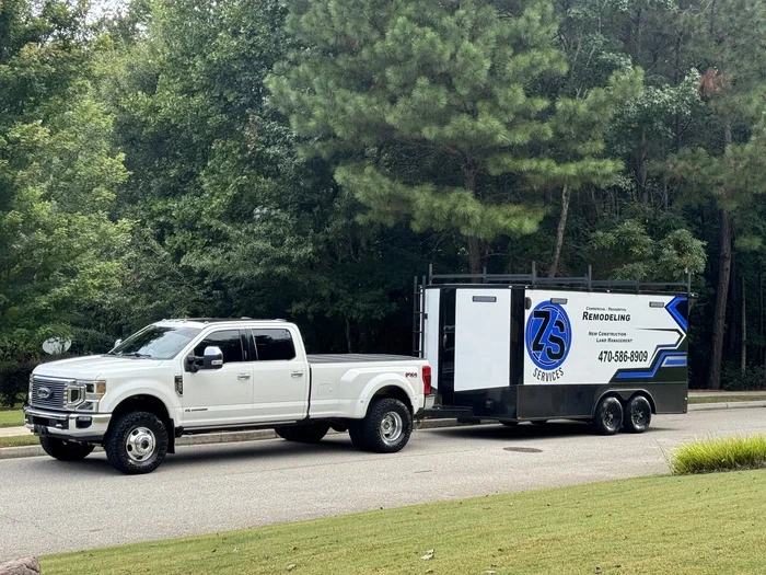 White pickup truck pulling a black and white service trailer on a road with trees in the background.