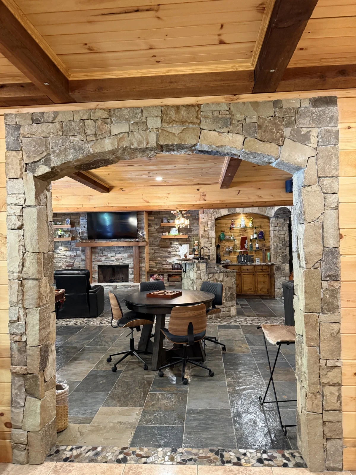 Living room with stone fireplace, wooden ceiling, and a dining area with chairs around a round table.