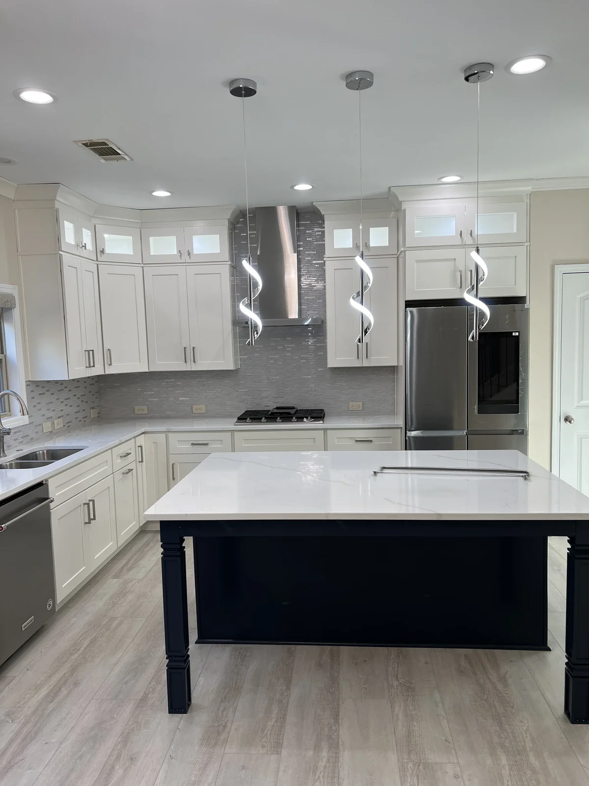Modern kitchen with white cabinets, gray backsplash, stainless steel appliances, a black kitchen island with a white countertop, and spiral pendant lights.