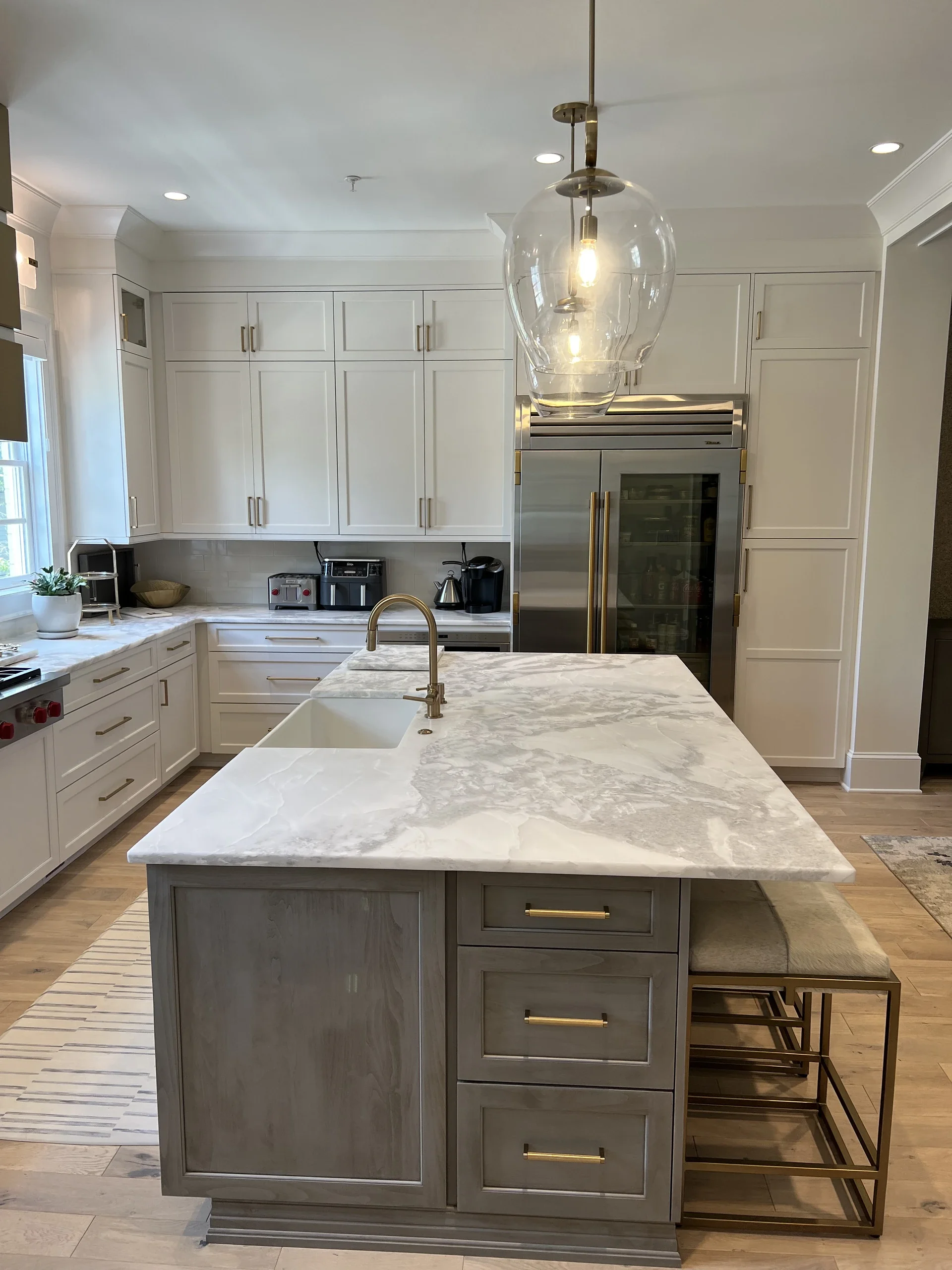 Modern kitchen with white cabinets, a marble island, pendant lighting, and stainless steel appliances.