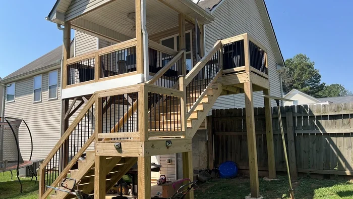 Newly built wooden deck and stairs attached to the back of a house with beige siding, in a residential backyard.