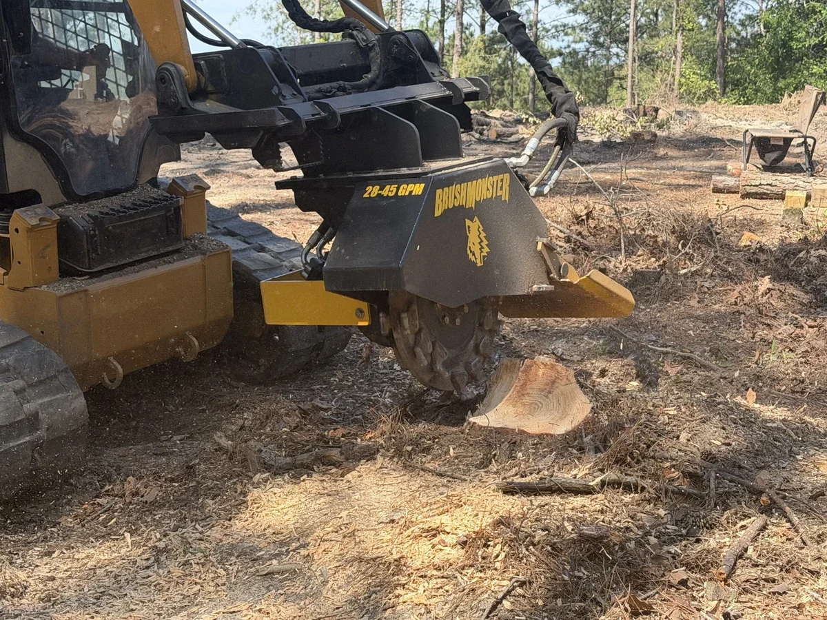 A stump being cut by a large brush cutting machine in a wooded area.