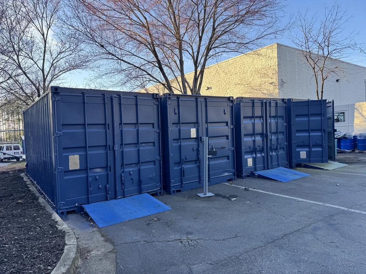 A large blue shipping container that is turned on its side in a parking lot, with accessible ramps for wheelchair entry.