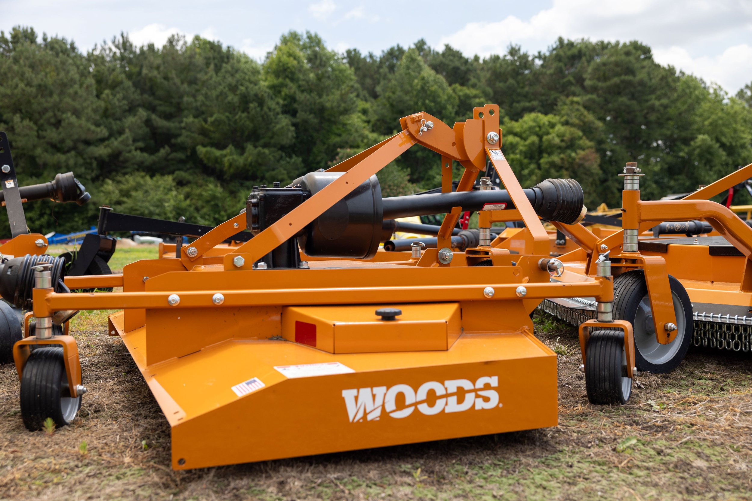 Orange Woods rotary mower on a grassy area with trees in the background.