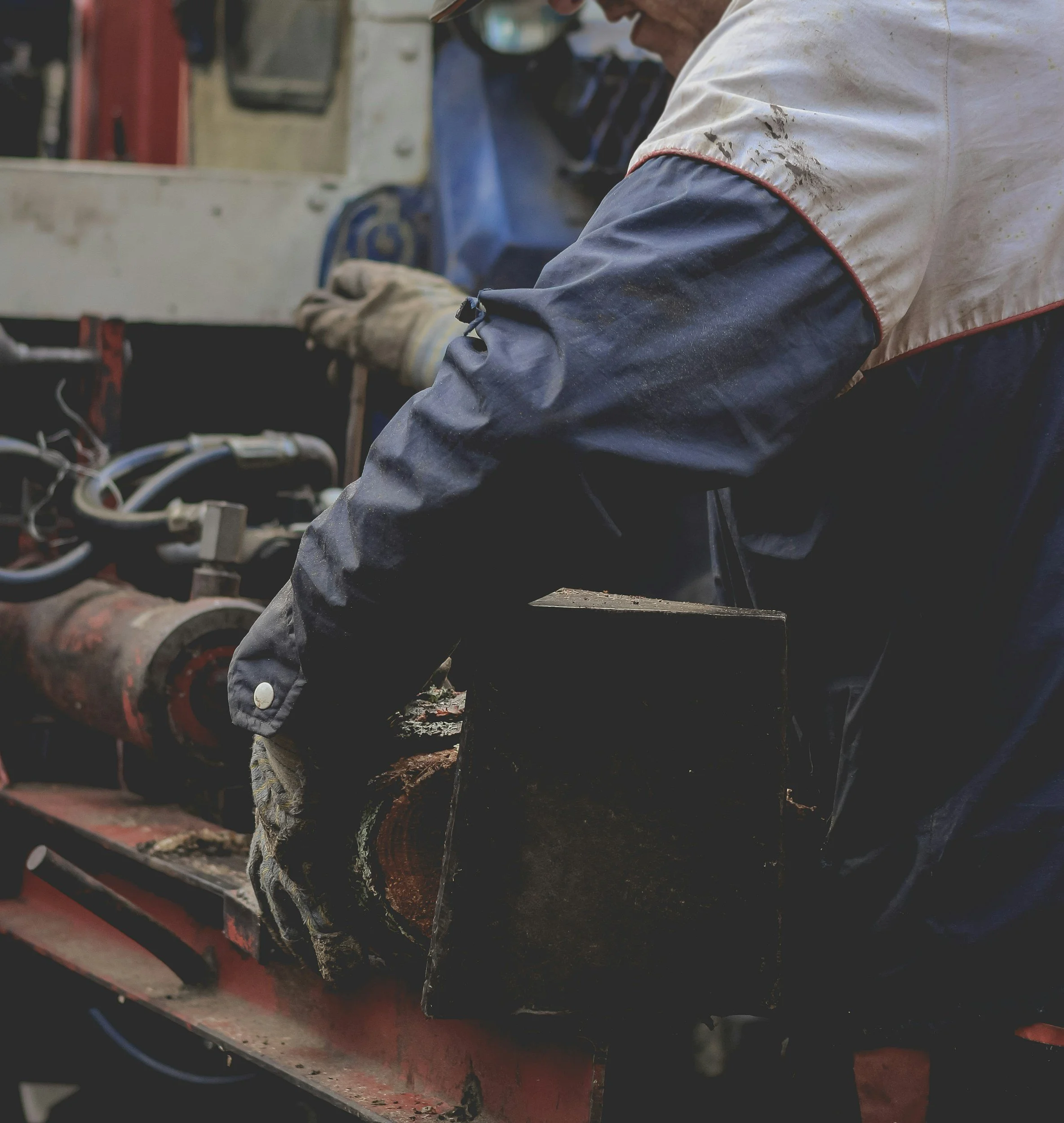 A worker in safety gear cuts a log with a chainsaw at a lumber yard or sawmill.