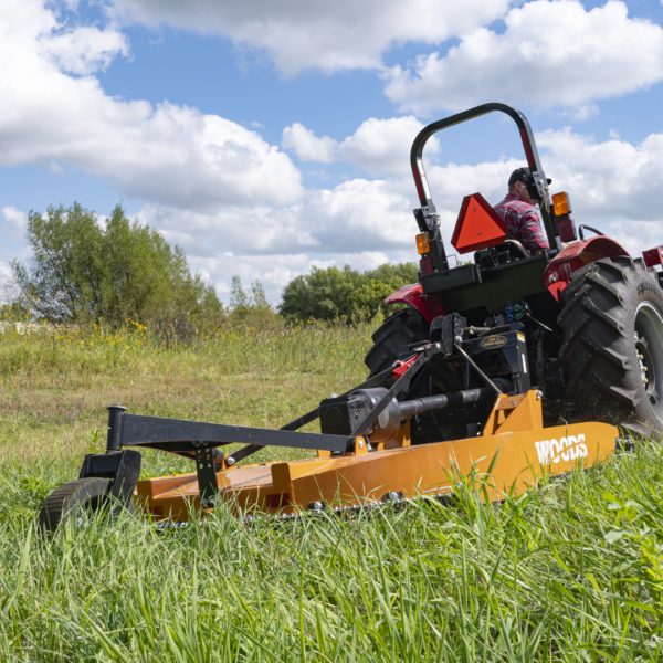 A man driving a tractor in a grassy field with trees and a cloudy sky in the background.