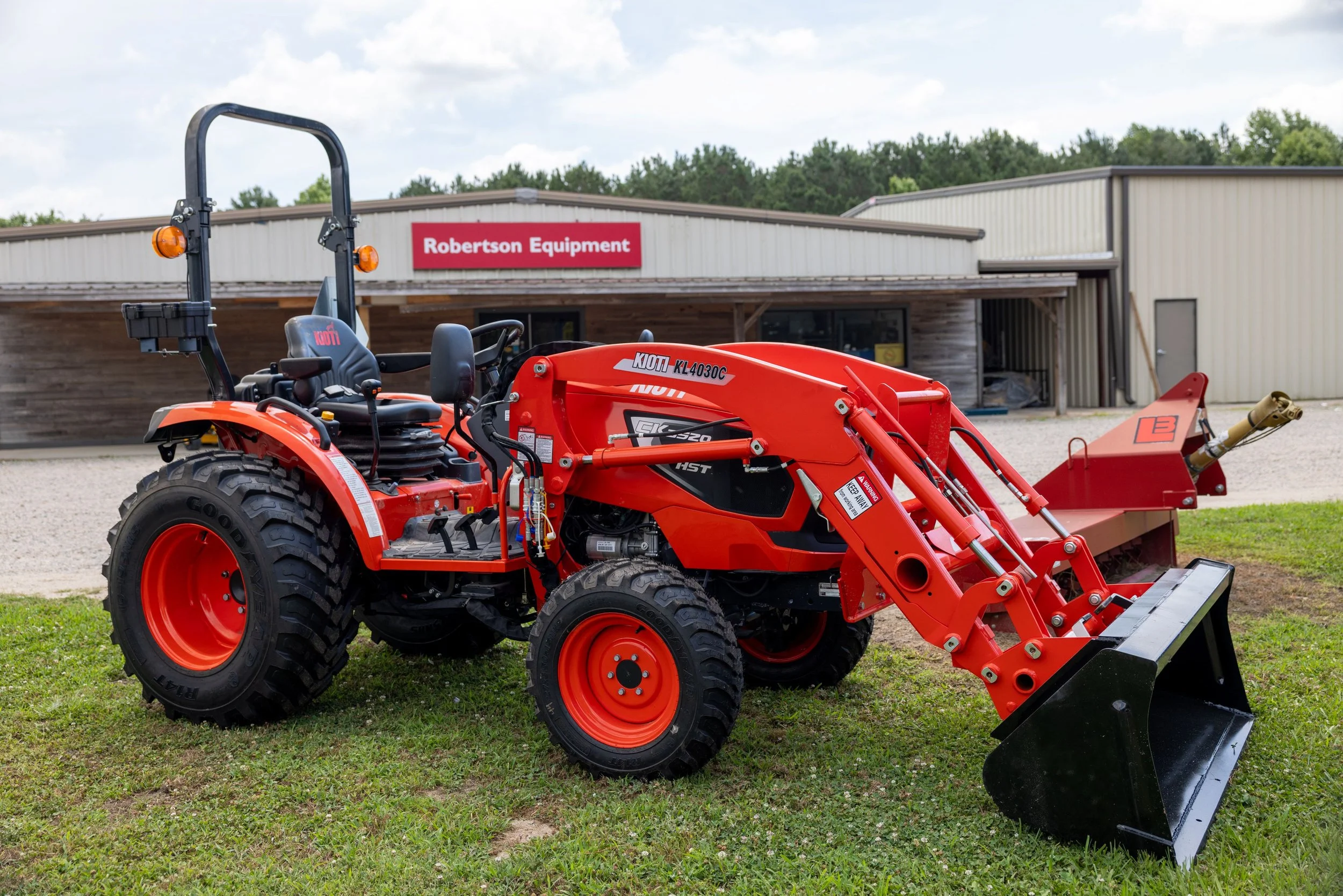 A red compact tractor with a front loader attachment in front of a building labeled Robertson Equipment.