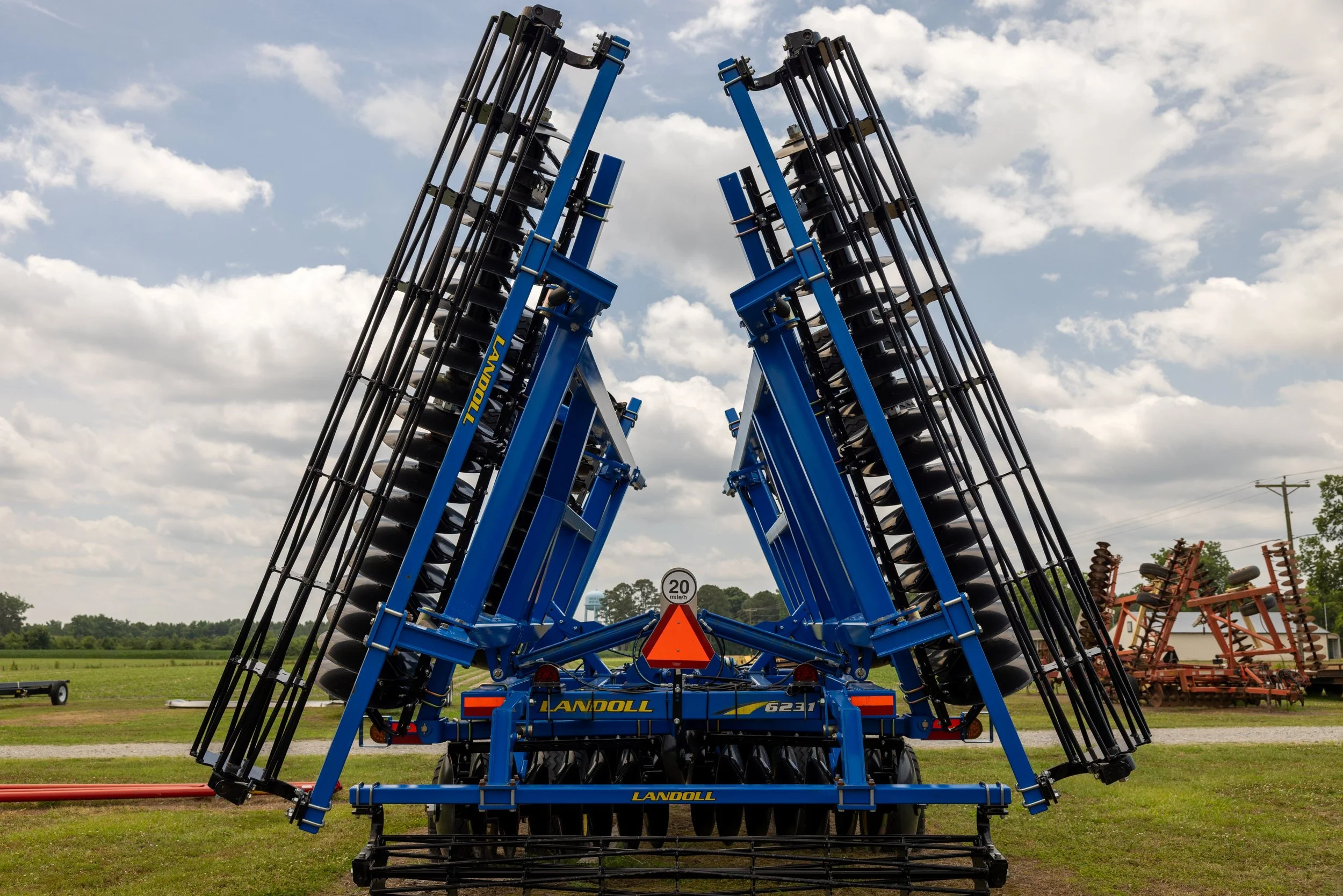Blue agricultural equipment with black rollers on a grassy field under a partly cloudy sky.