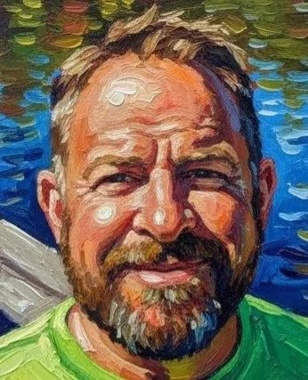 Portrait of a smiling man with a beard and mustache, wearing a green shirt, with water in the background.
