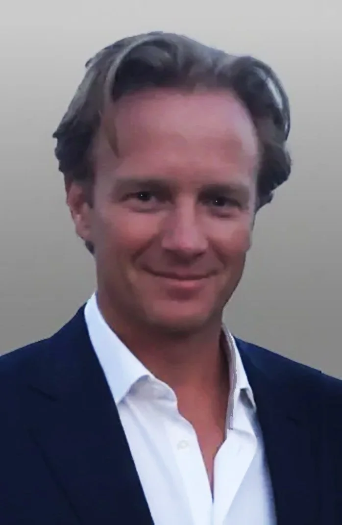 Headshot of a man with dark brown hair, wearing a white shirt and a dark blazer, smiling at the camera.
