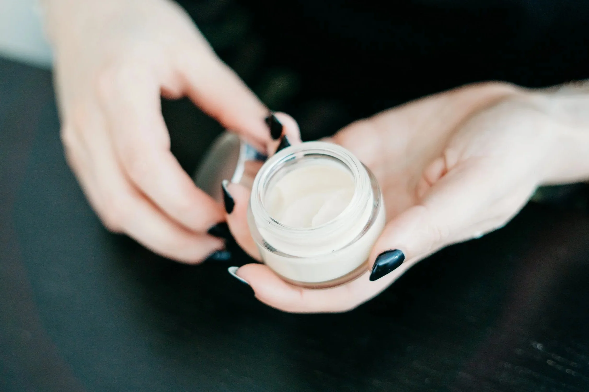 Close-up of a person's hands holding a small glass jar filled with a skincare formula.