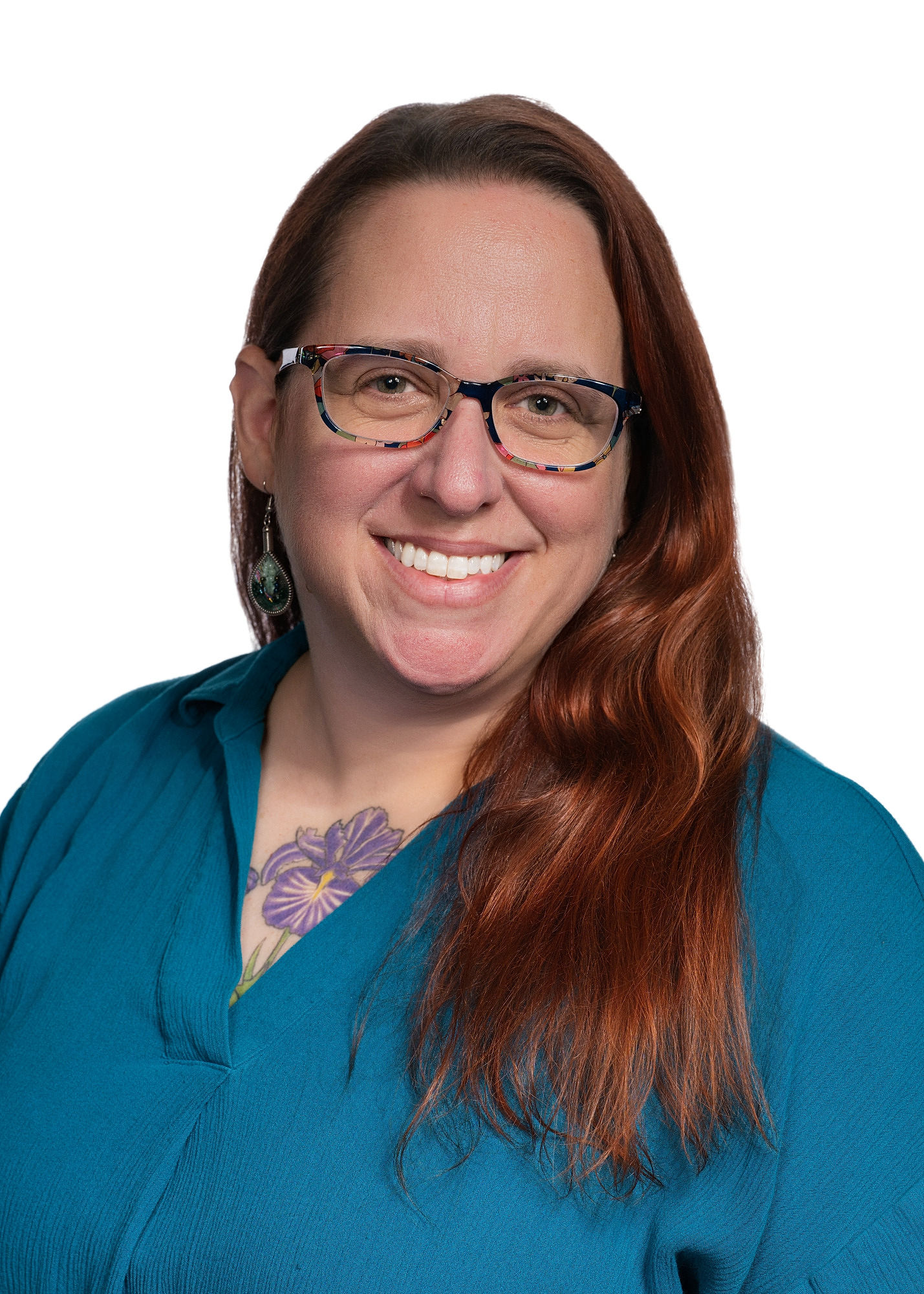 A portrait of Dr. Elizabeth Pietralczyk. She is smiling warmly into the camera. She has long red hair, multicolored glasses, and a tattoo of a purple iris can be seen above the neckline of her teal shirt.