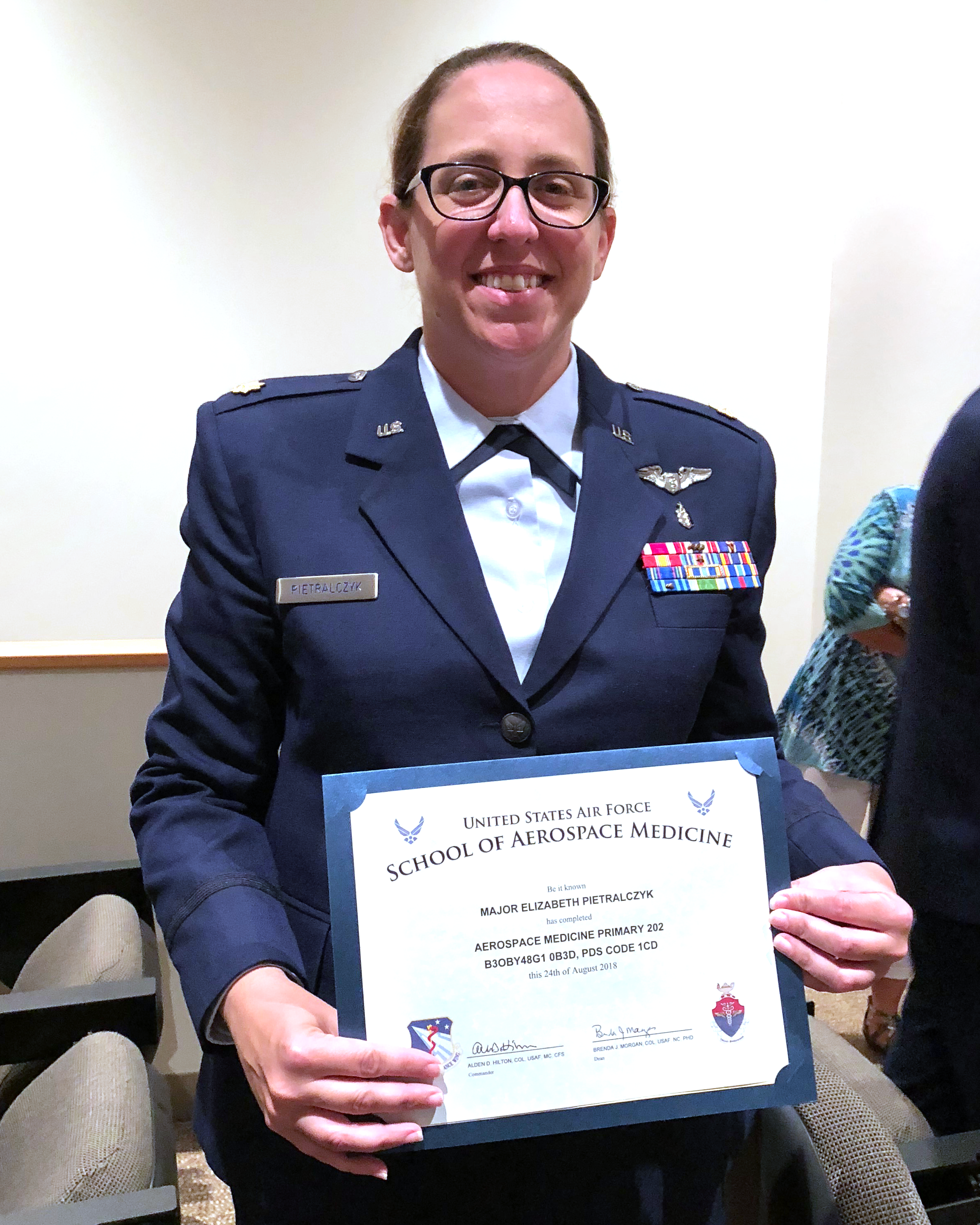 Doctor Liz holds her degree in Aerospace Medicine Primary from the United States Air Force School of Aerospace Medicine. She is wearing her blue Air Force uniform and smiling.