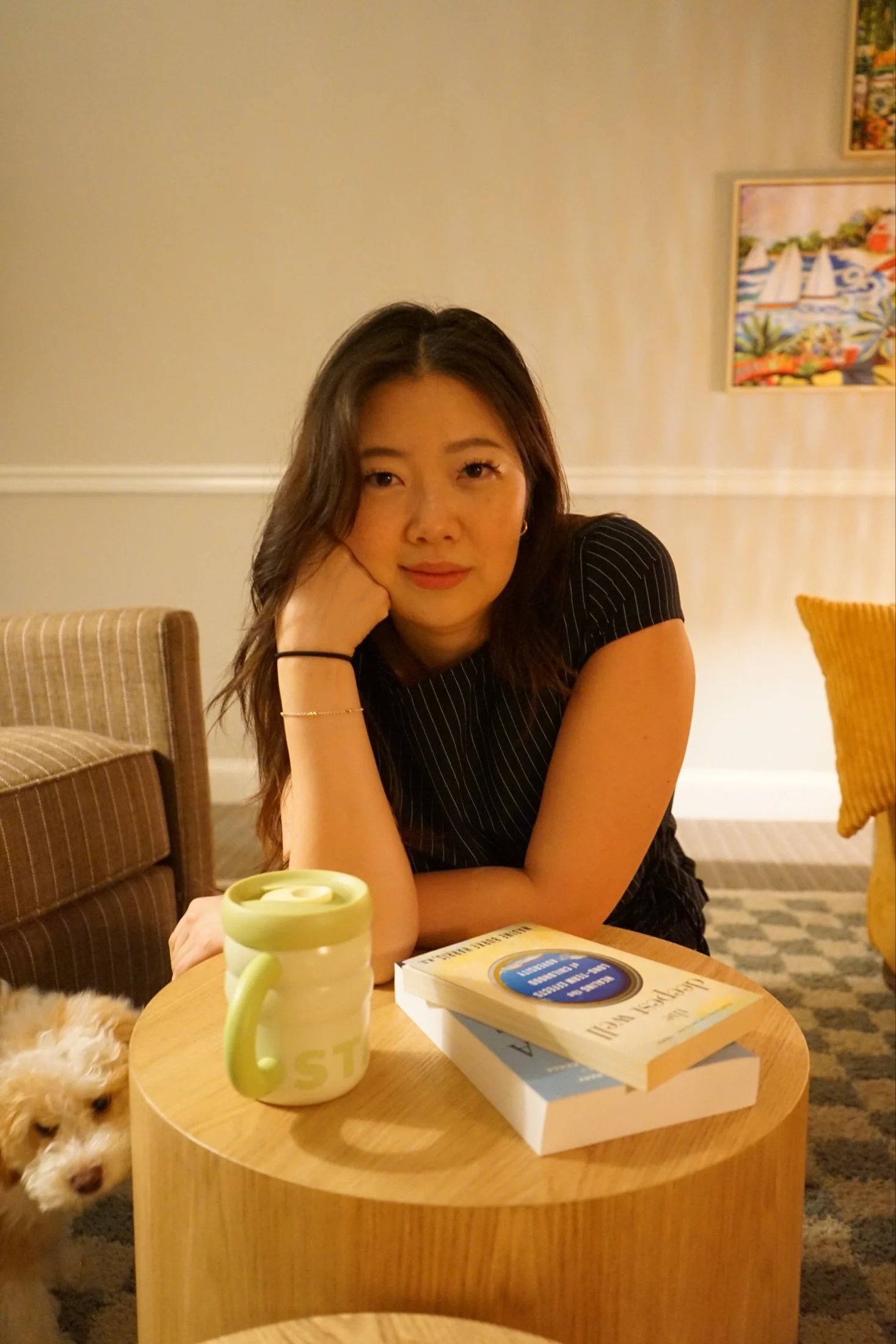 Cindy Song, LCSW, smiling at a table in her therapy office with her puppy nearby