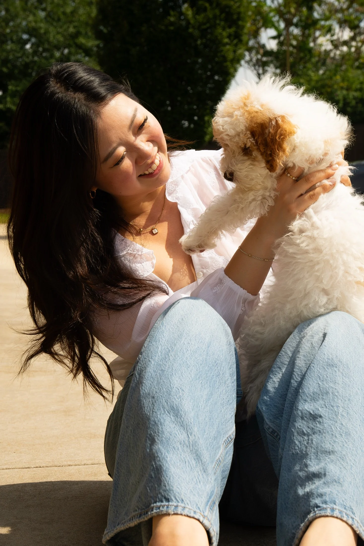 Cindy sitting outdoors, laughing as her puppy reaches up to her