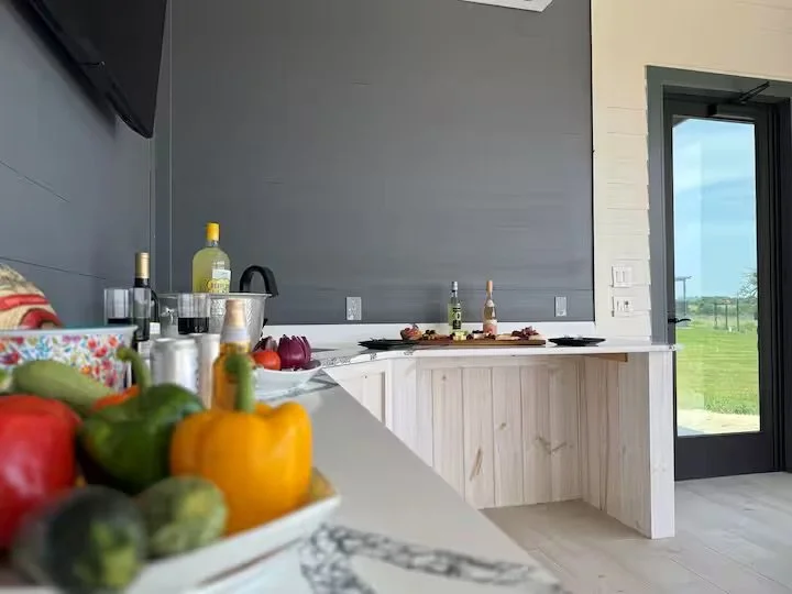 Kitchen with white counter, various vegetables, bottles of oil, and a dish with food on the counter near a window and door to the outside.