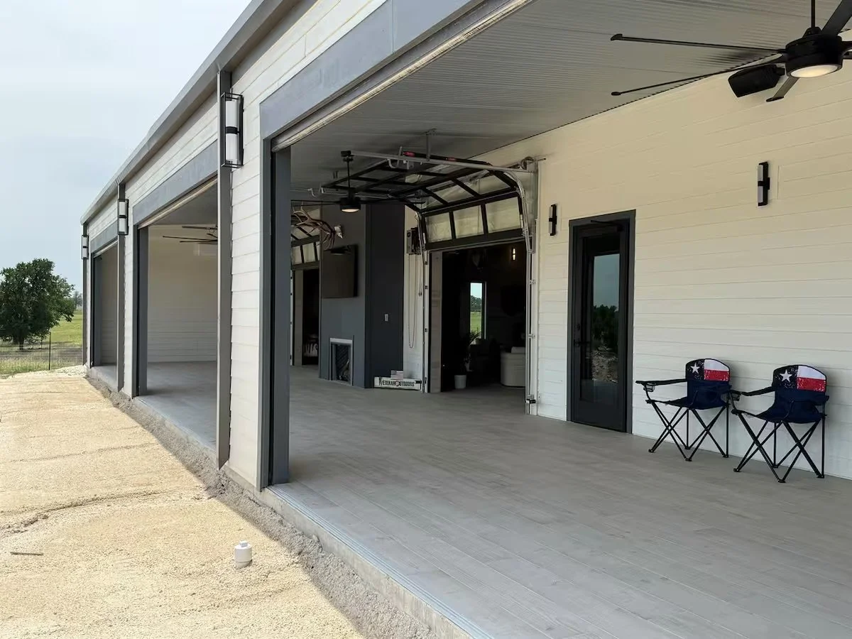 A partially open garage with a modern interior, two black chairs with patriotic designs on the right, a ceiling fan, and a view to the outdoors with a tree in the distance.