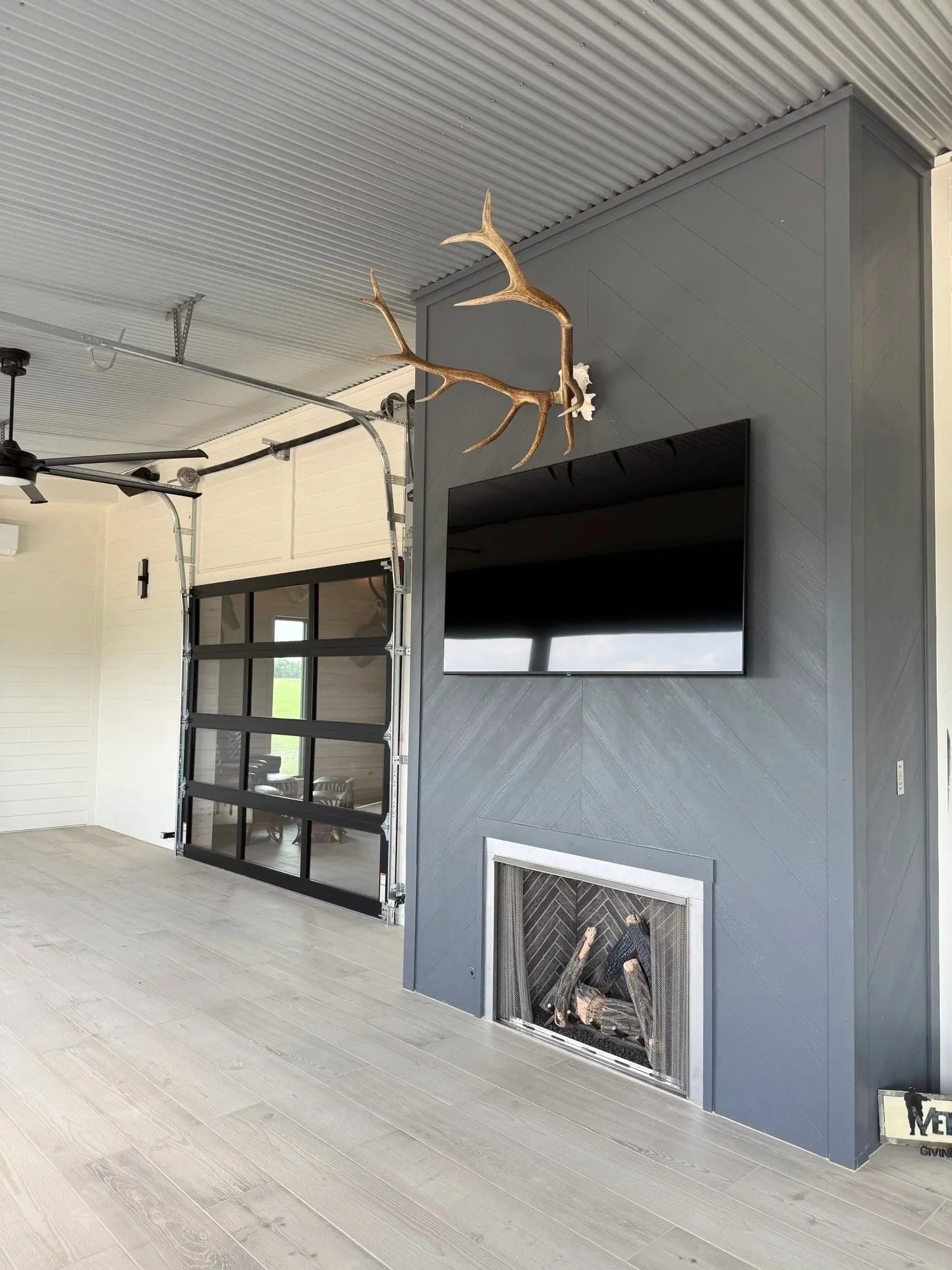Interior of a modern living room with a stone fireplace, mounted flat-screen TV, ceiling fan, and decorative antlers on the wall.