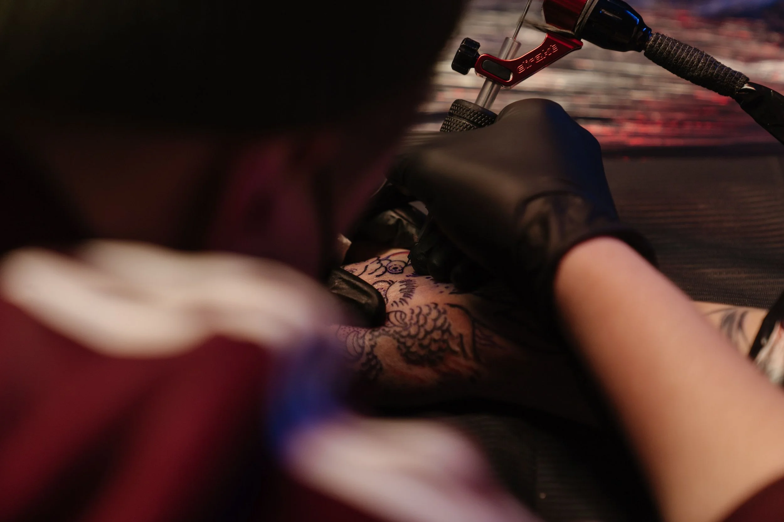 Close-up of a person riding a motorcycle on a dark road, showing their gloved hand on the handlebar and part of their arm with tattoos.
