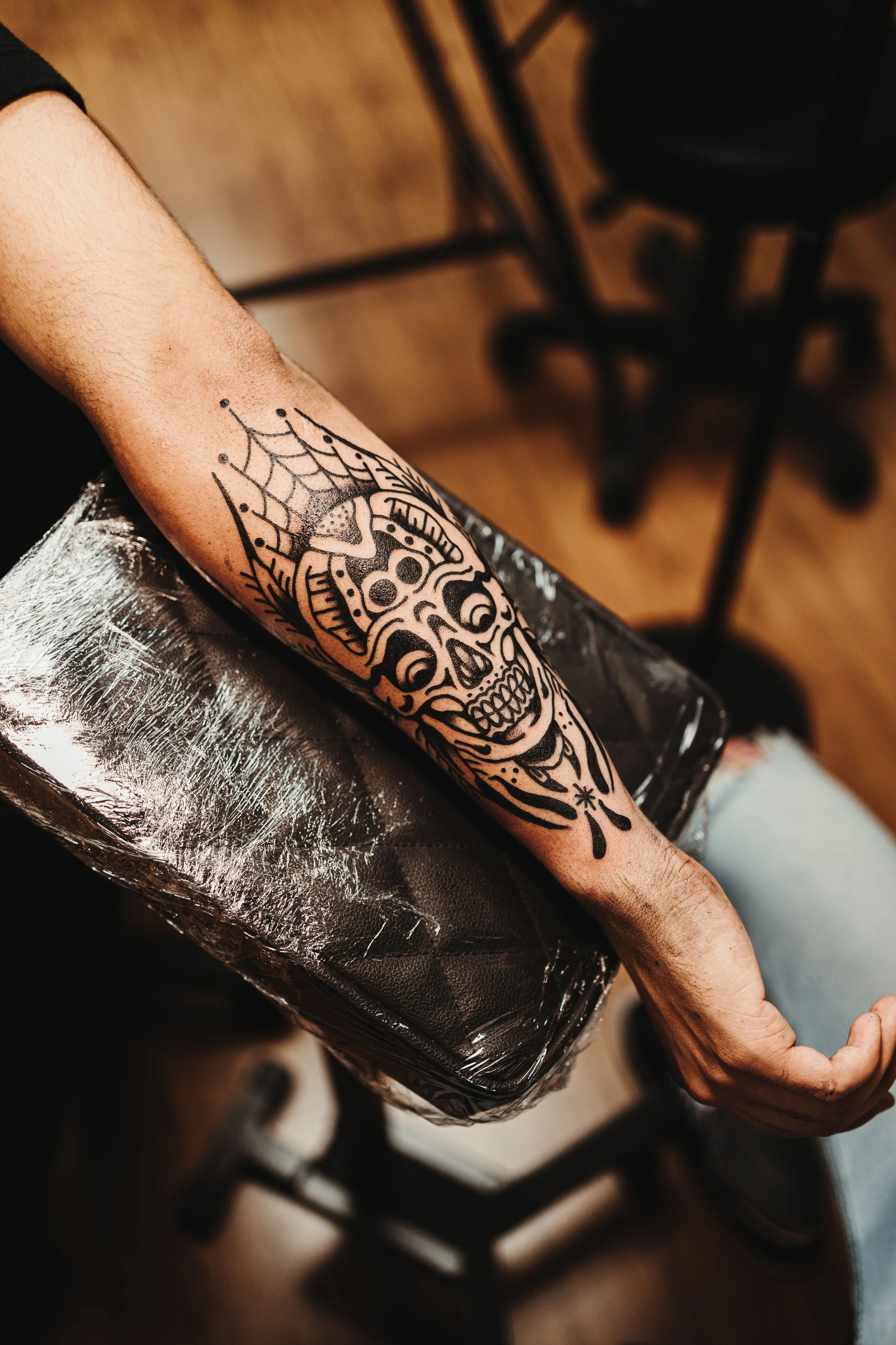 A person's forearm with a black tattoo of a stylized skull with floral and abstract design elements.