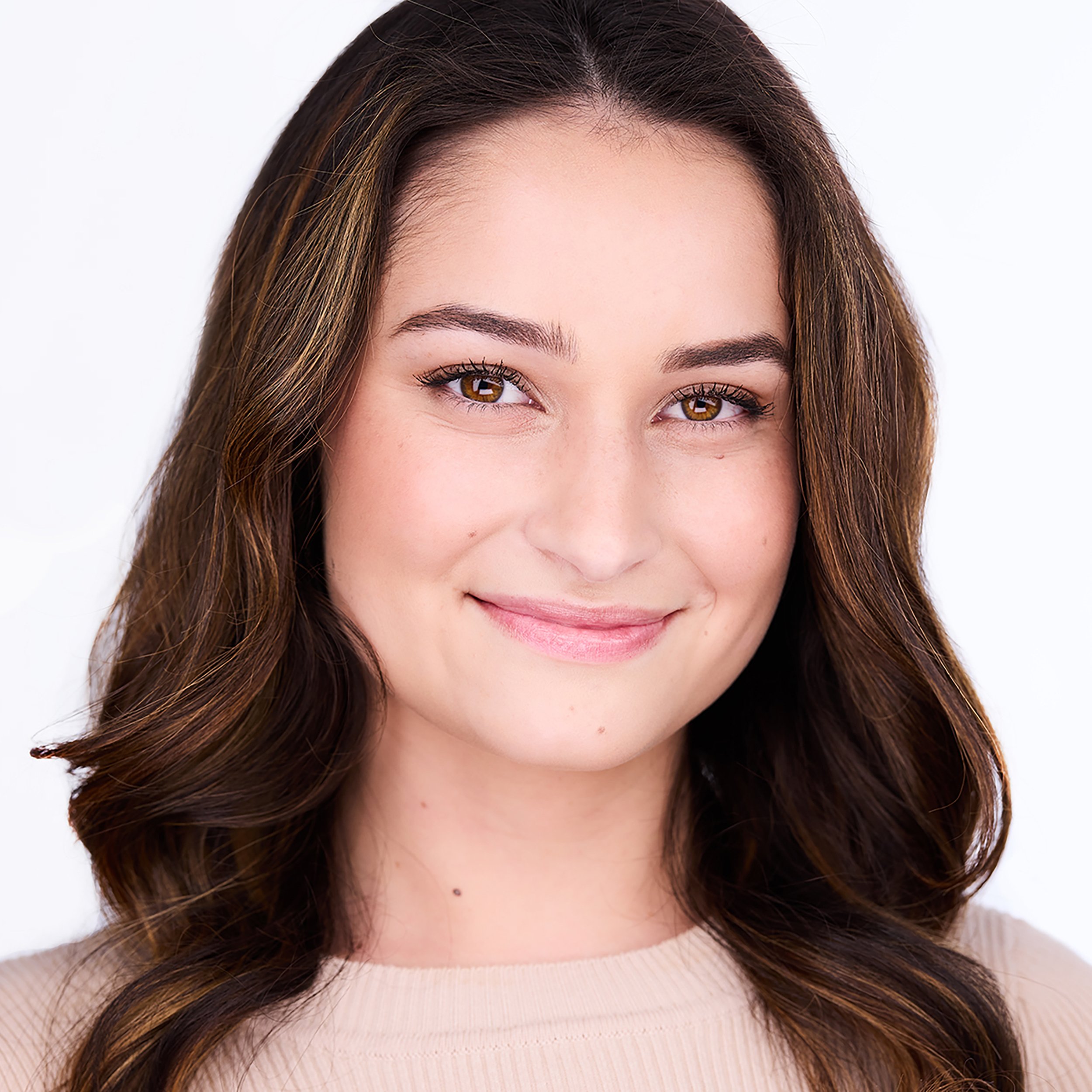 Close-up of a woman's face showing her forehead, eyes, and part of her nose and mouth. She has brown hair with subtle highlights, well-groomed eyebrows, and is smiling slightly.