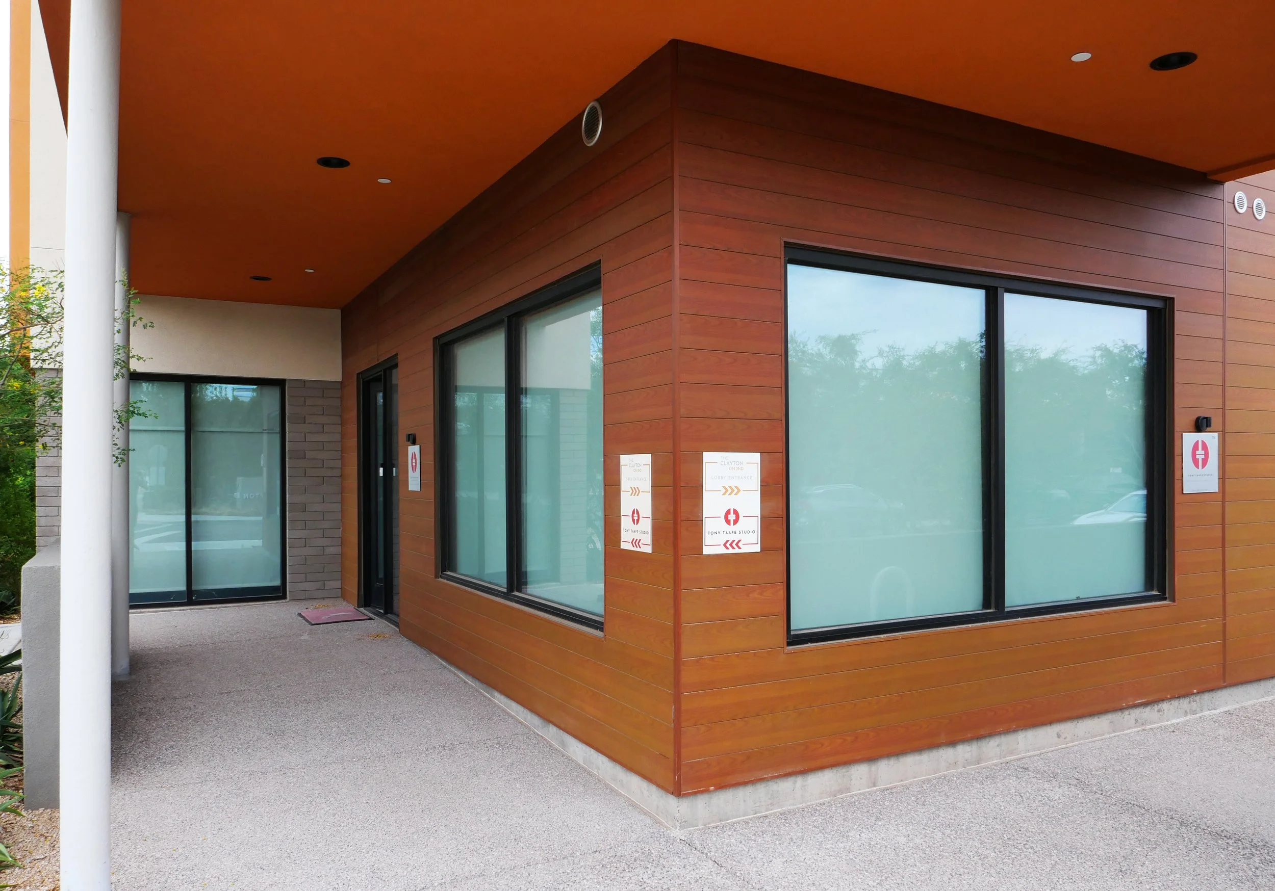 Tony Taafe Studio in Scottsdale with wooden siding, large frosted glass windows, and a colorful overhanging roof. There are signs near the door with a red cross and directional arrows.